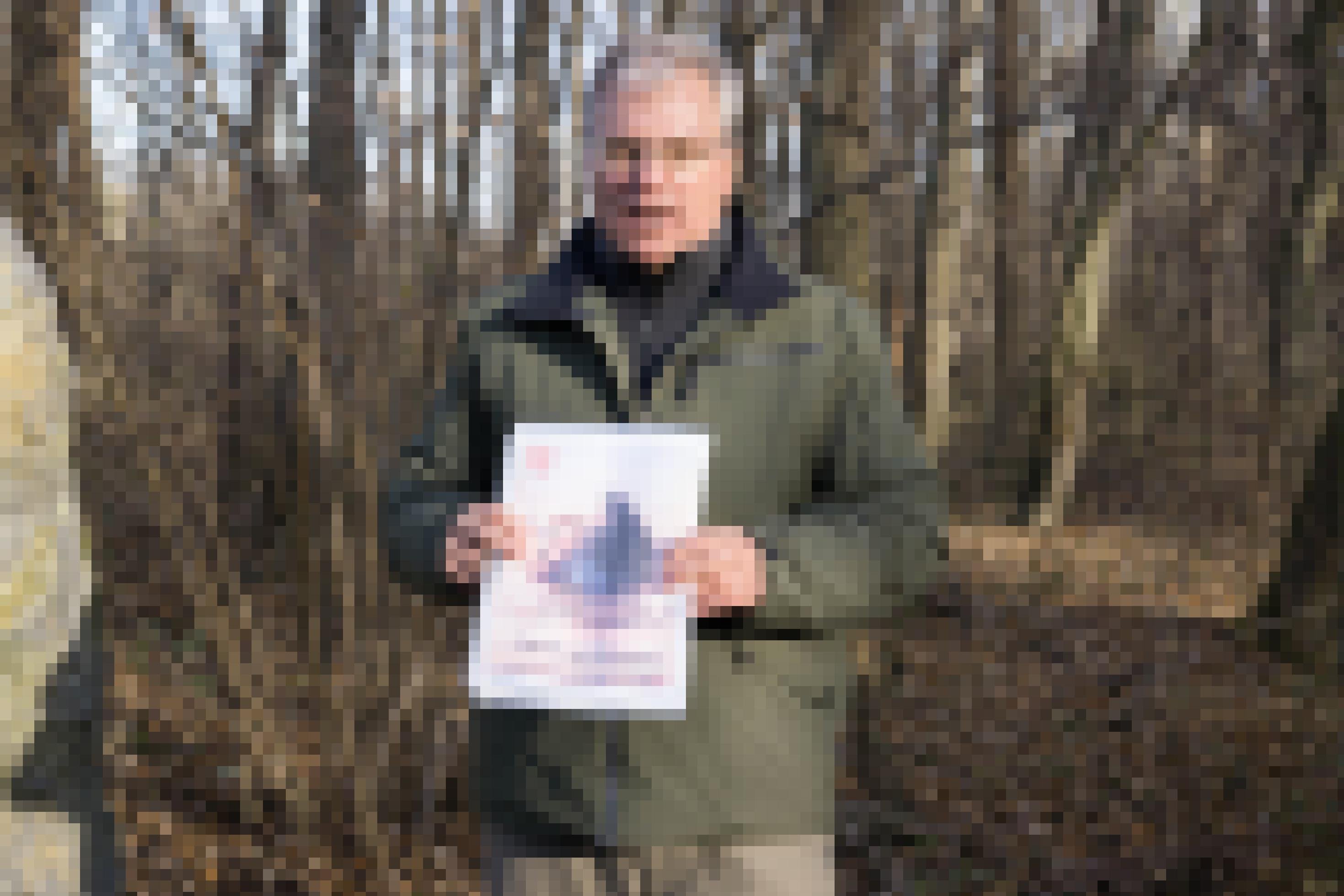 Mann steht in der Au und hält Zeitungscover in der Hand.