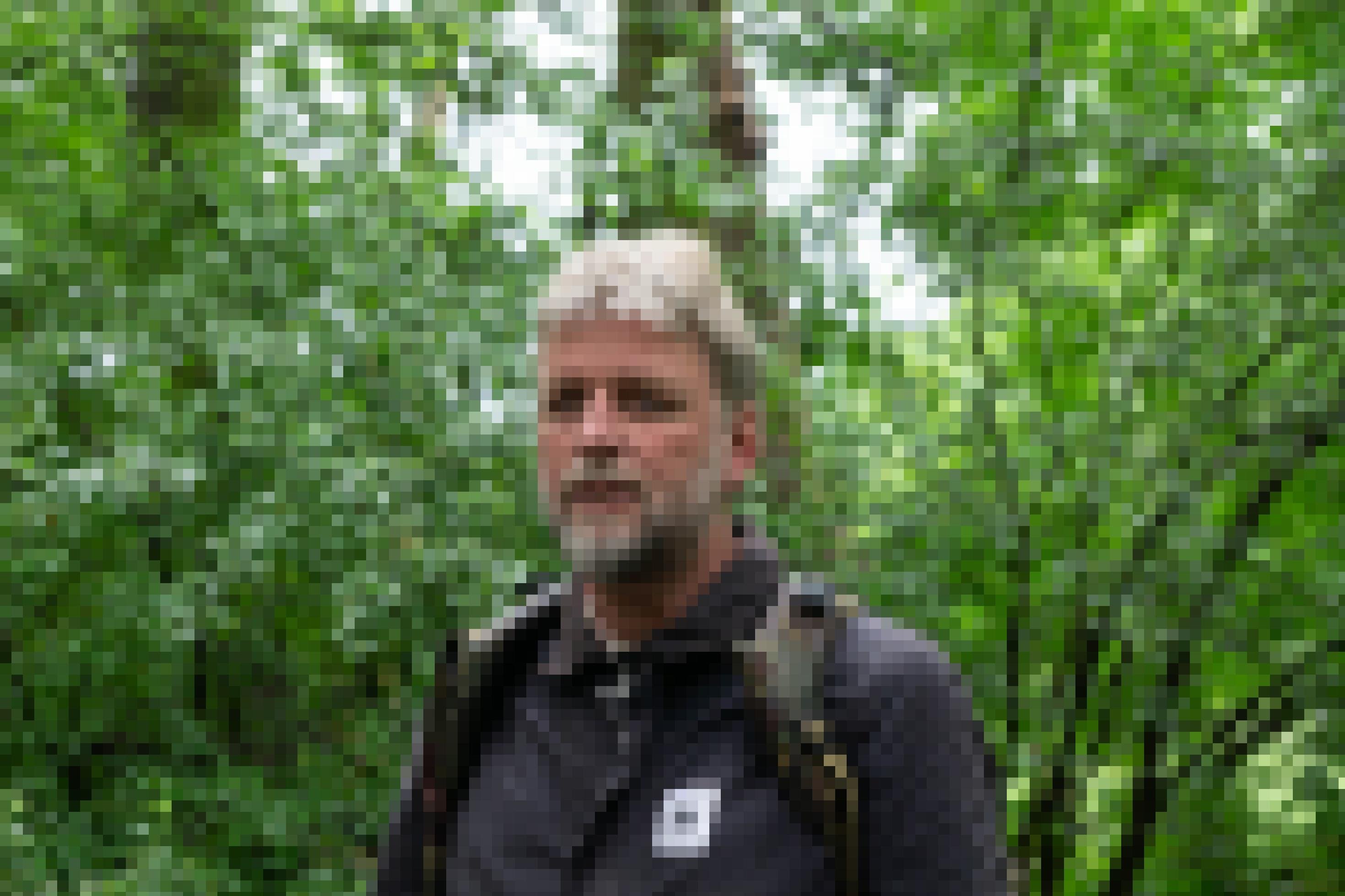 Mann mit weißem Haar und Bart steht im Auwald