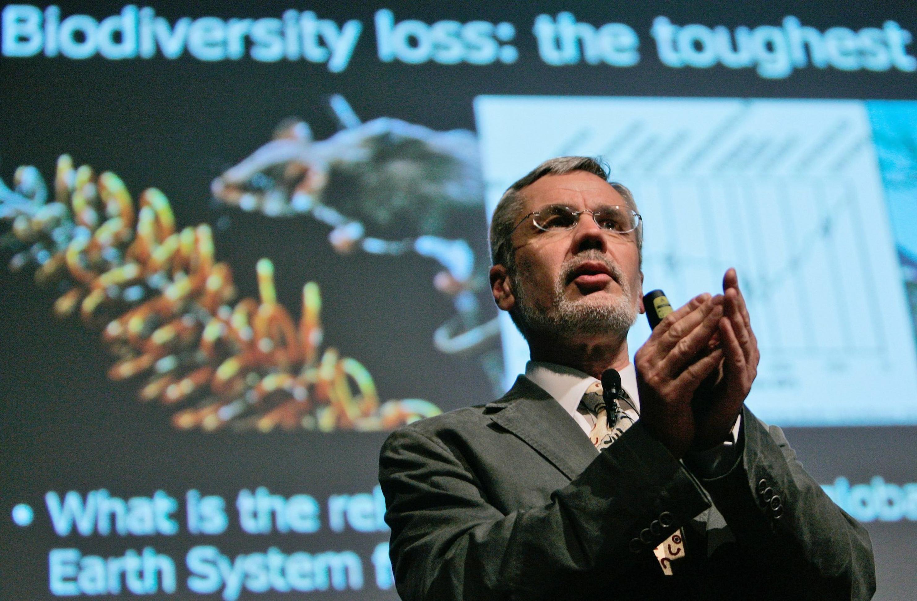 Steffen hat als Redner die Hände gefaltet. Hinter ihm ist eine projizierte Folie zu sehen, auf der das Wort Biodiversität steht.