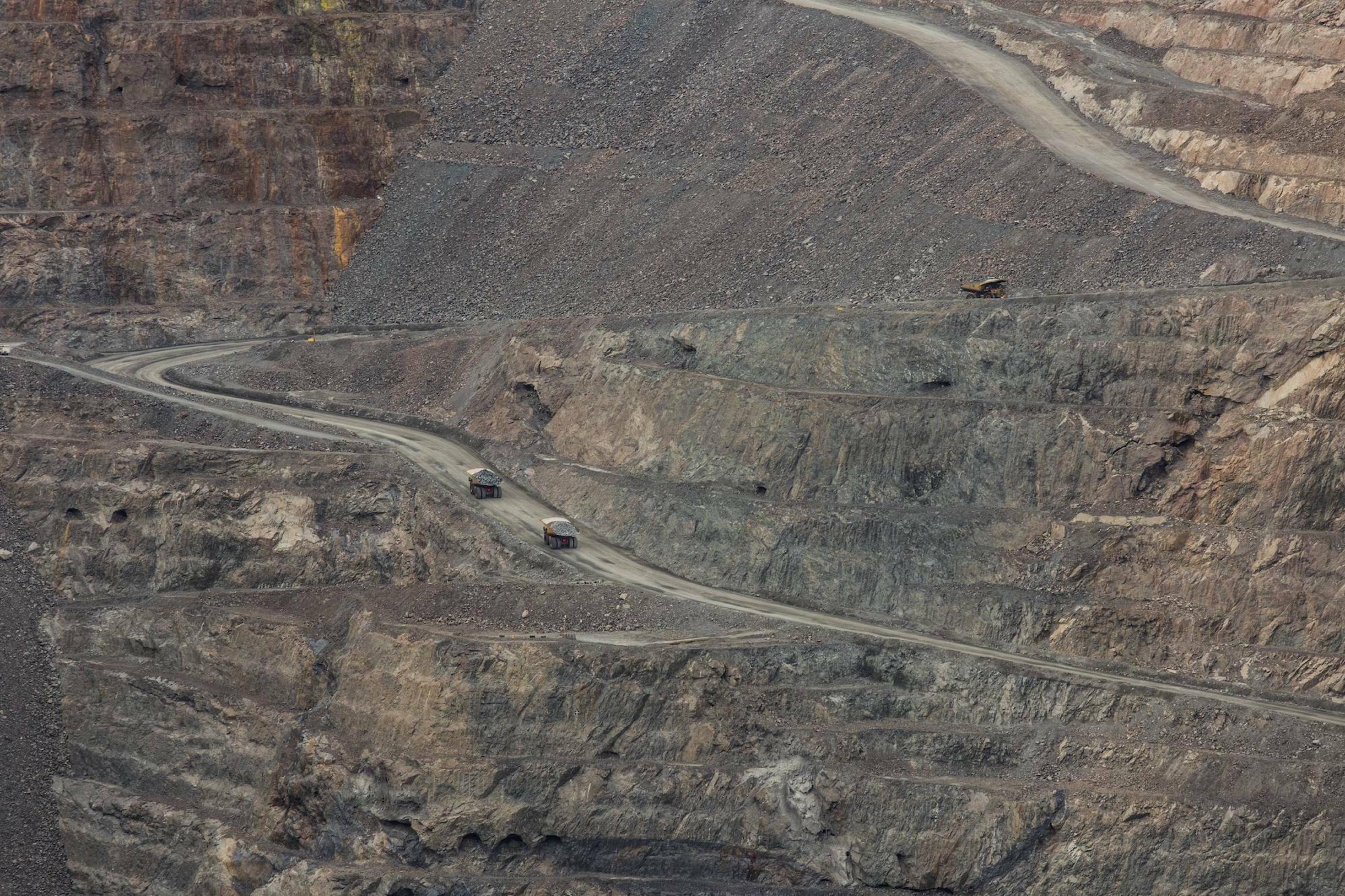 Das Bild zeigt die Kohlmine in der Fernansicht, ein riesiges Loch in der Landschaft, durch das zwei klein wirkende Lastwagen fahren.