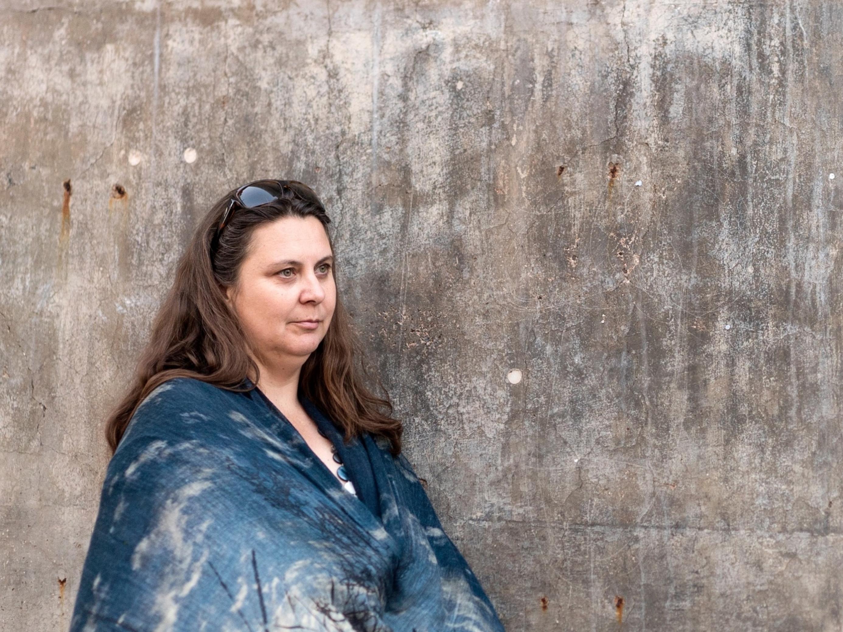 Auf dem Bild steht die Klimaforscherin Nerilie Abram in ein schönes blaues Tuch gehüllt vor einer kahlen Betonwand. Sie schaut nachdenklich in die Ferne.