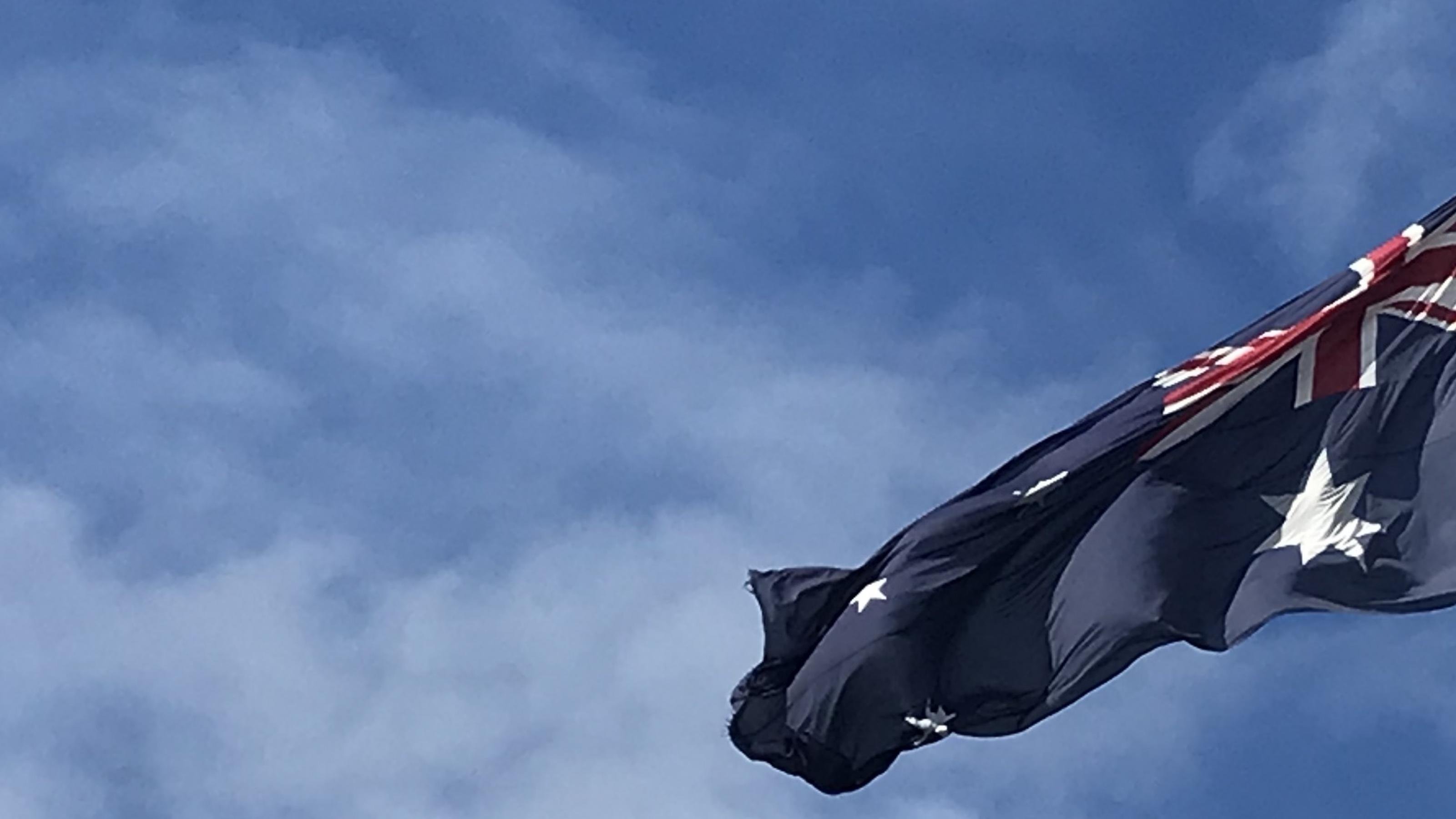 Eine Australische Flagge weht über einem Shoppingcenter vor blauem Himmel.