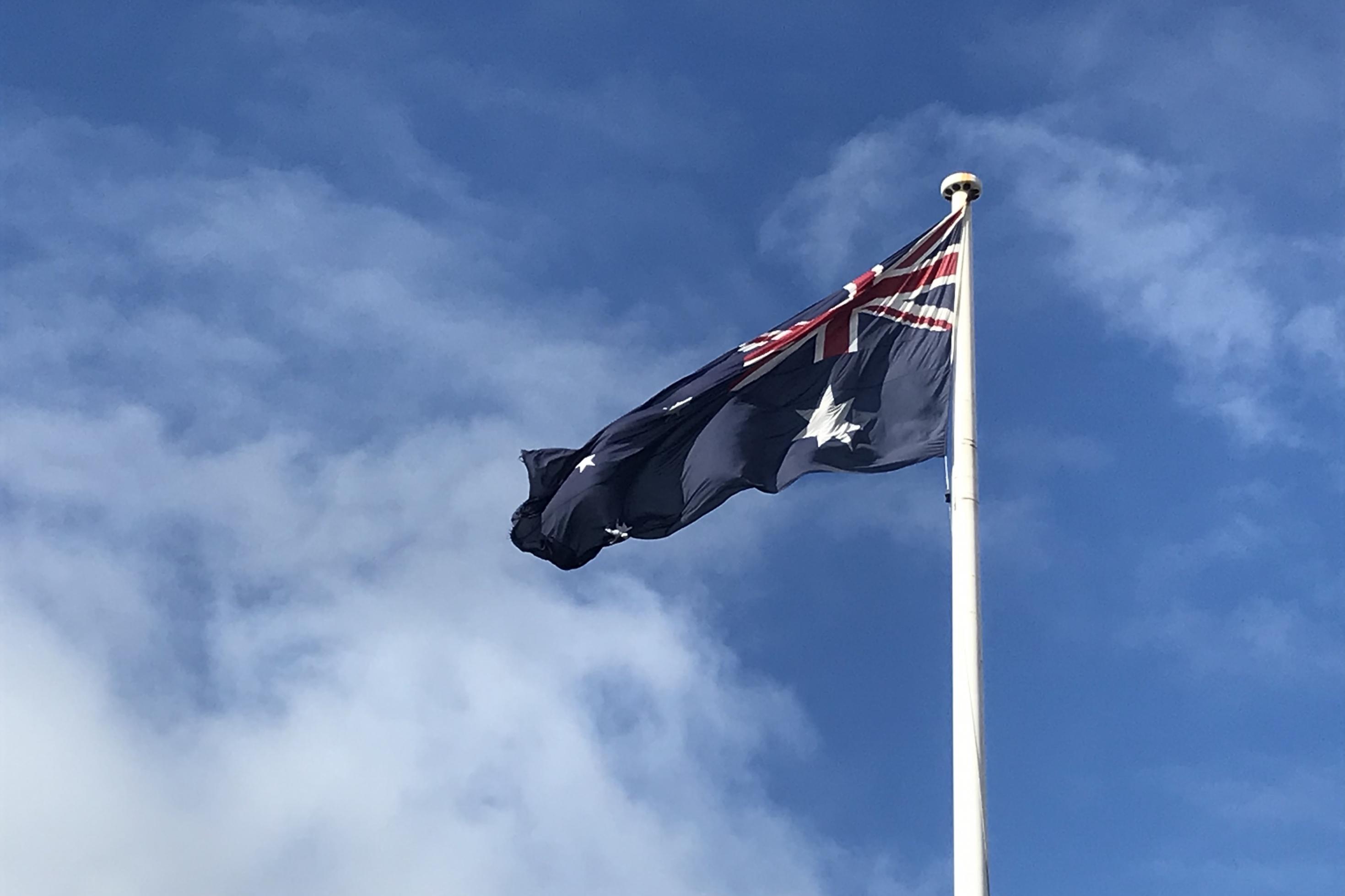 Die australische Flagge weht an einem Mast vor blauem Himmel