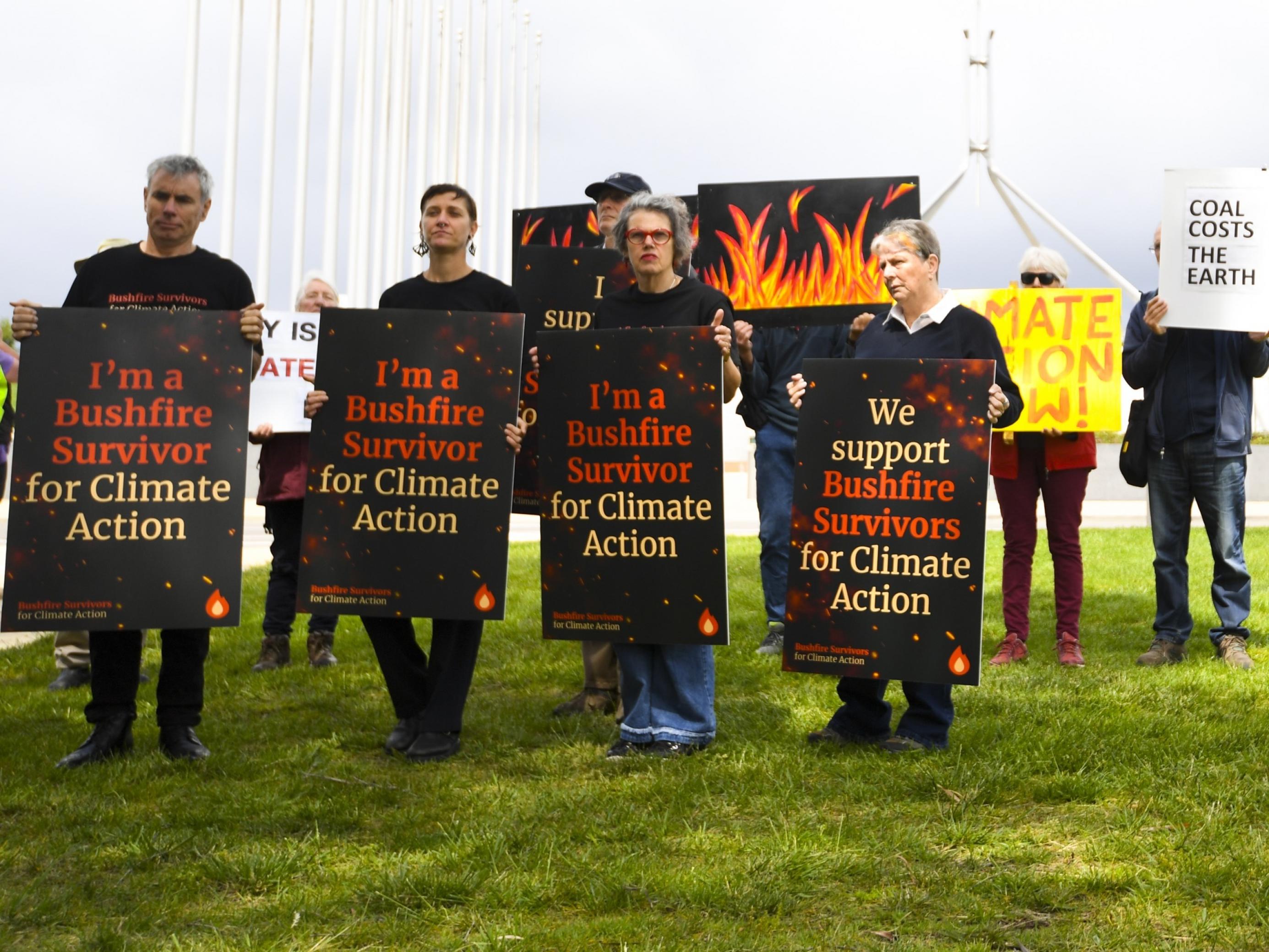 Demonstrantïnnen, die sich als Überlebende der Bushfire bezeichnen, fordern mit Schildern, dass die Regierung beim Klimaschutz endlich handelt.
