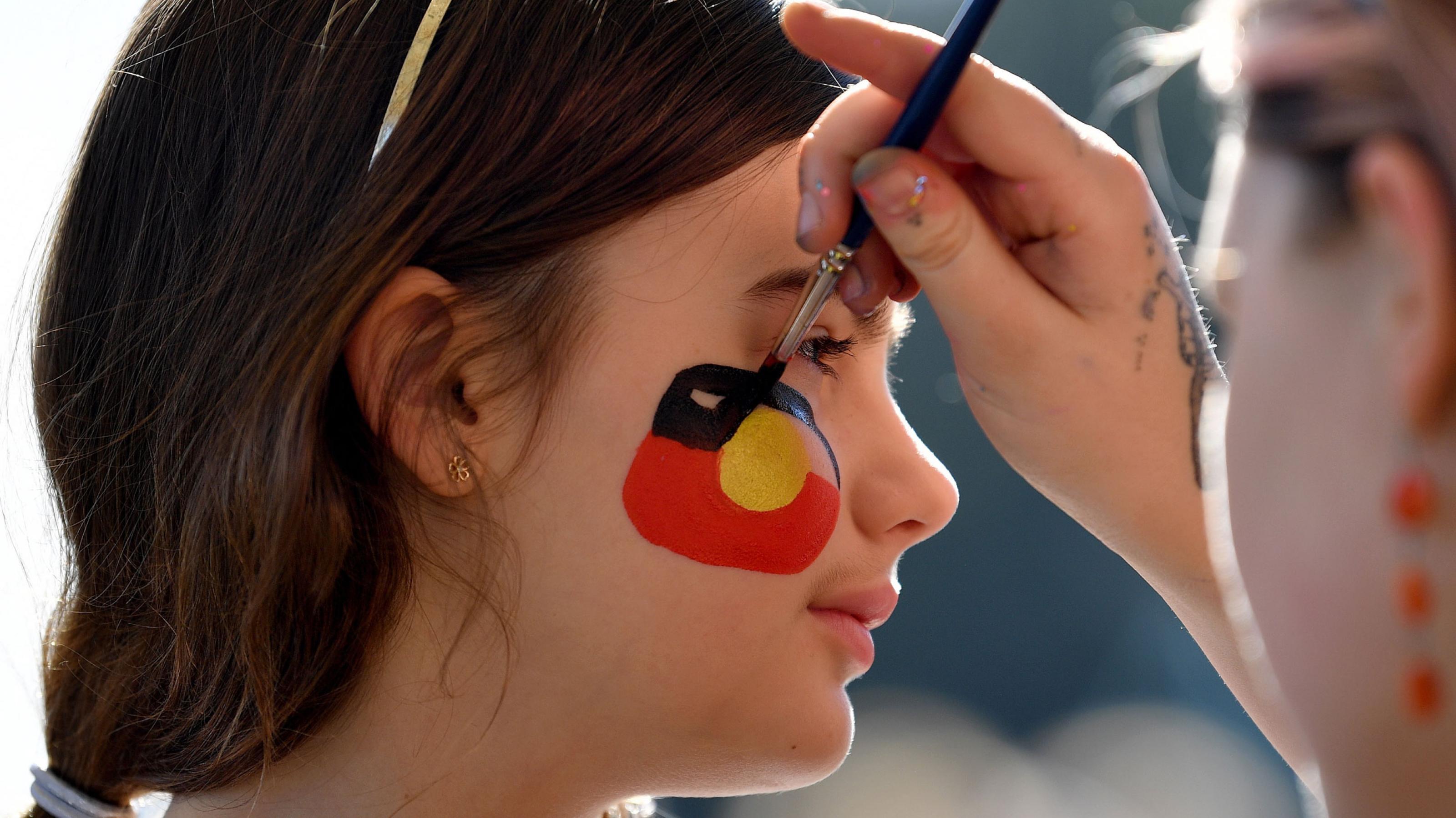 Bei einer Informationsveranstaltung der „Yes 23“-Kampagne lässt sich ein Mädchen in Sydney eine Aboriginal-Flagge in den Farben Rot Schwarz und Gold auf die Wange malen.