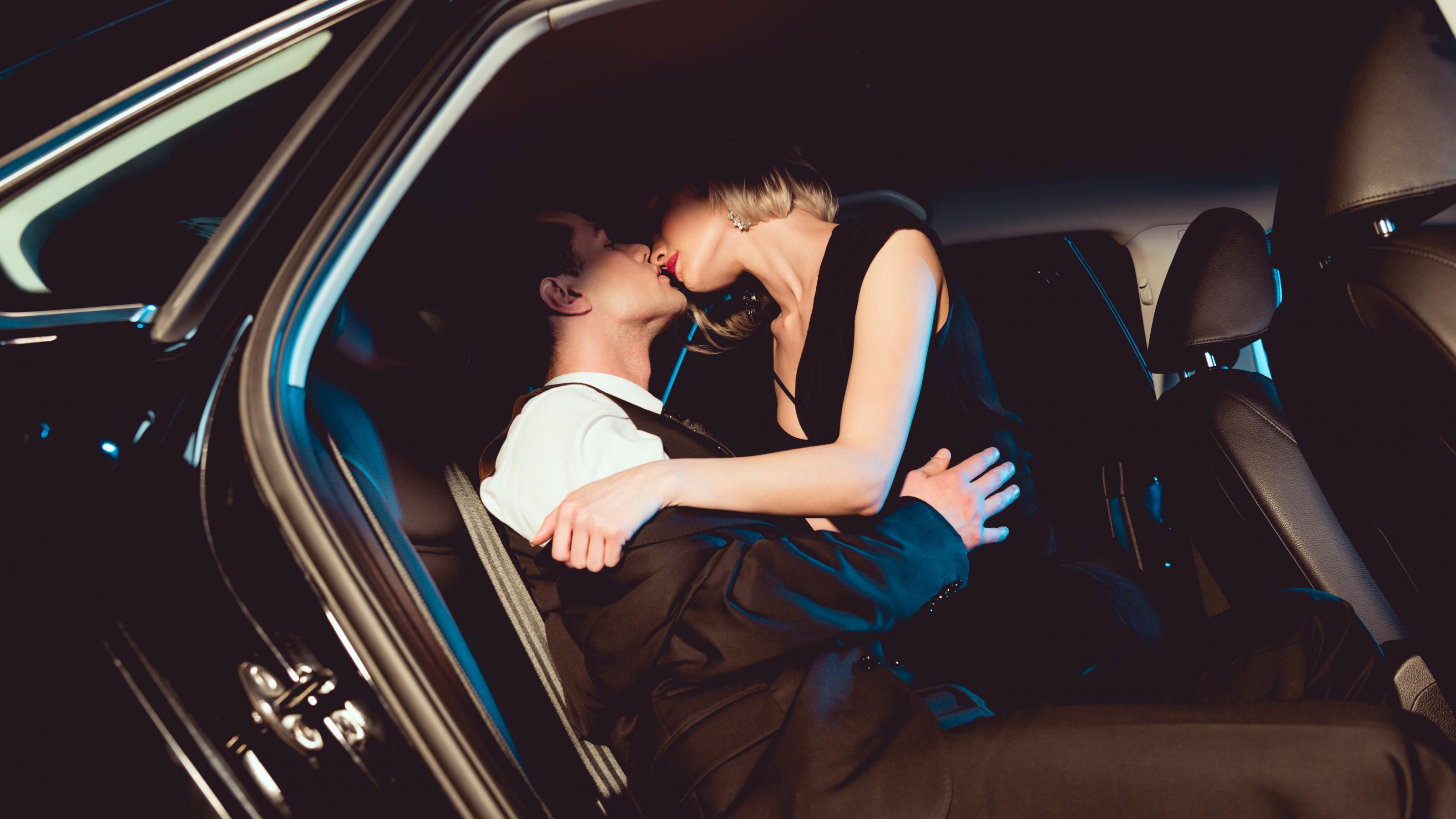 Stilvoll gekleideter Mann küsst junge Frau auf der Rückbank eines Autos