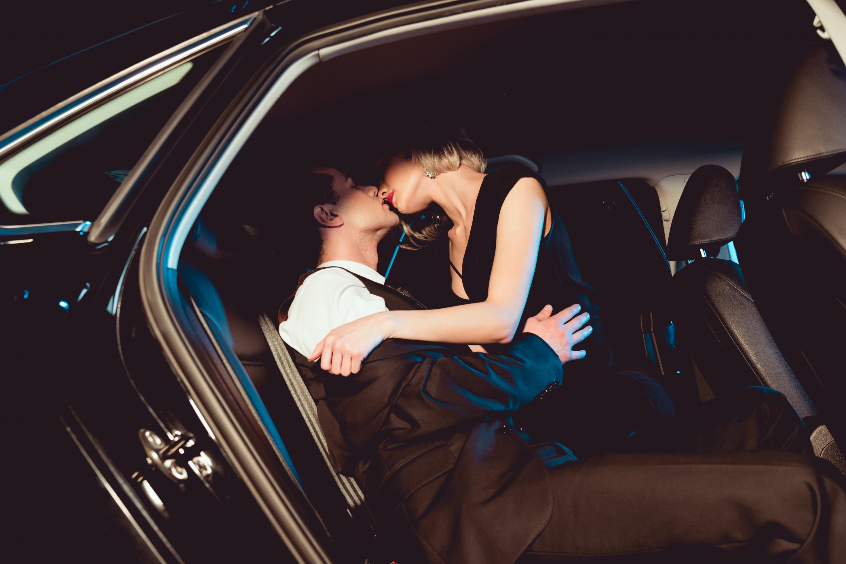 Stilvoll gekleideter Mann küsst junge Frau auf der Rückbank eines Autos