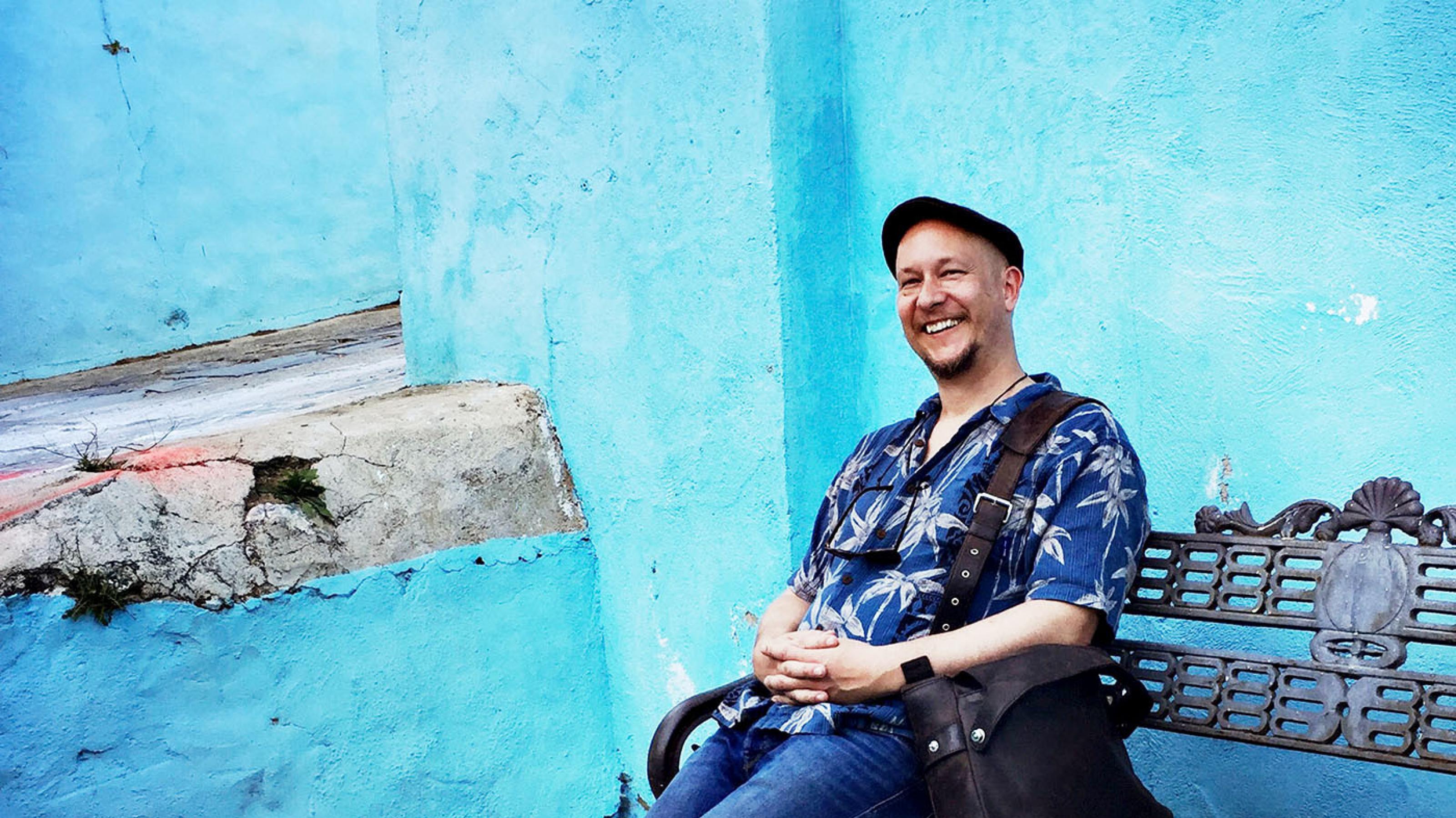 Der Autor und Fotograf Björn Göttlicher sitzt auf einer Bank vor einer blauen Wand