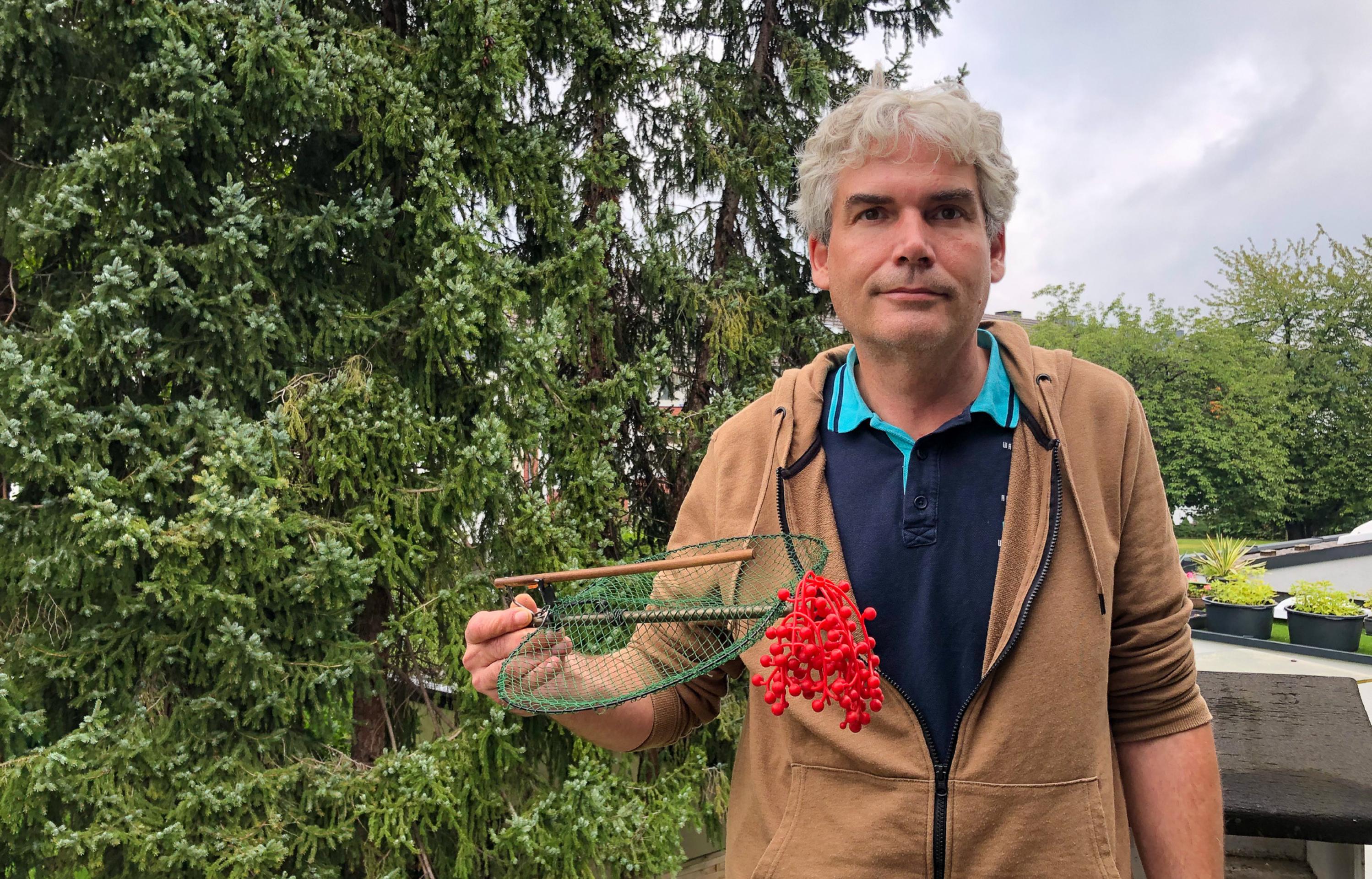 Ein Mann hält eine Konstruktion mit zwei Dratbügeln in der Hand. Sie sind mit einem feinen Netz überspannt und durch eine Feder verbunden.