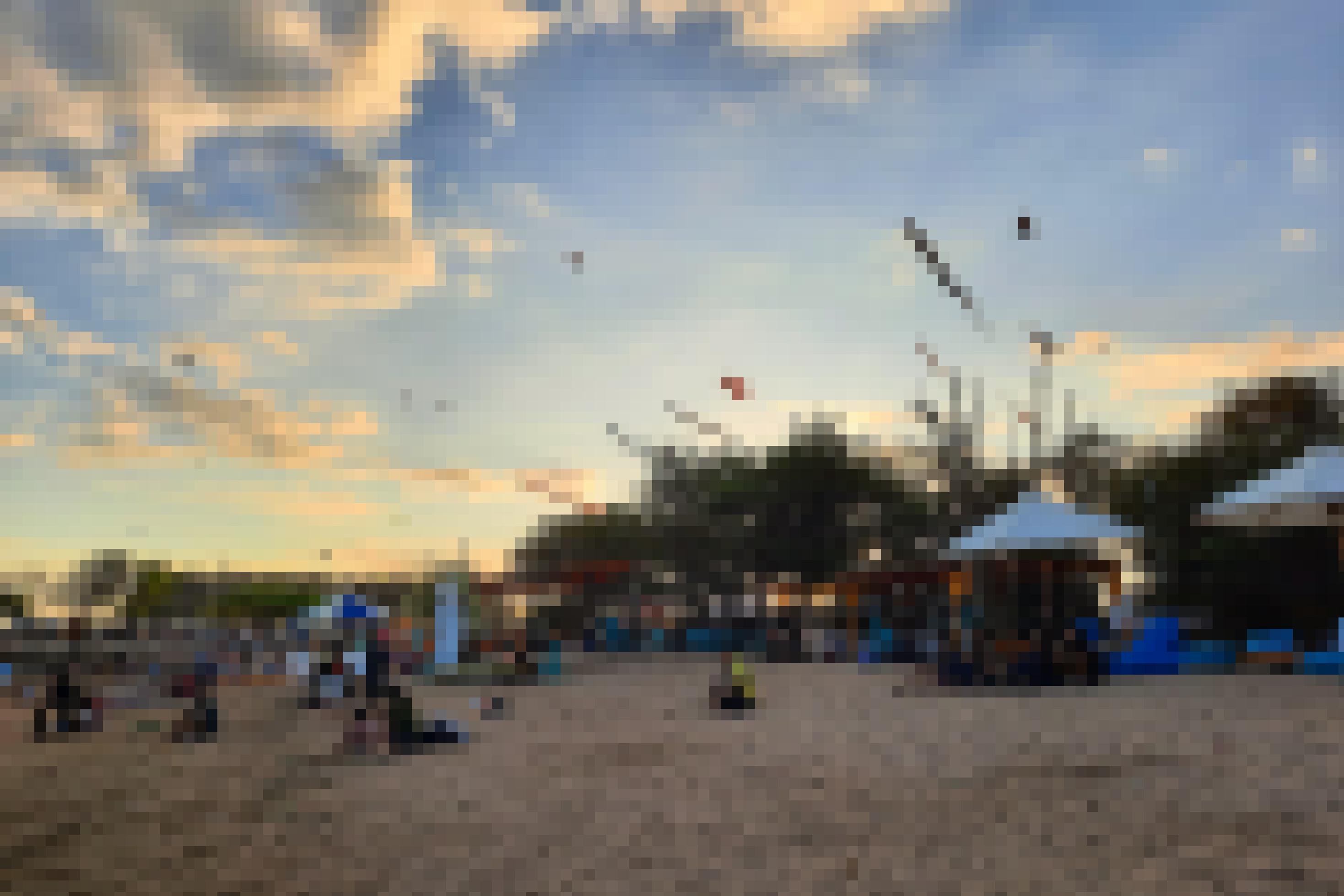 Am Mertasari-Strand in Sanur sitzen Indonesier*innen am Sand. Am Himmel sind Flugdrachen zu sehen.