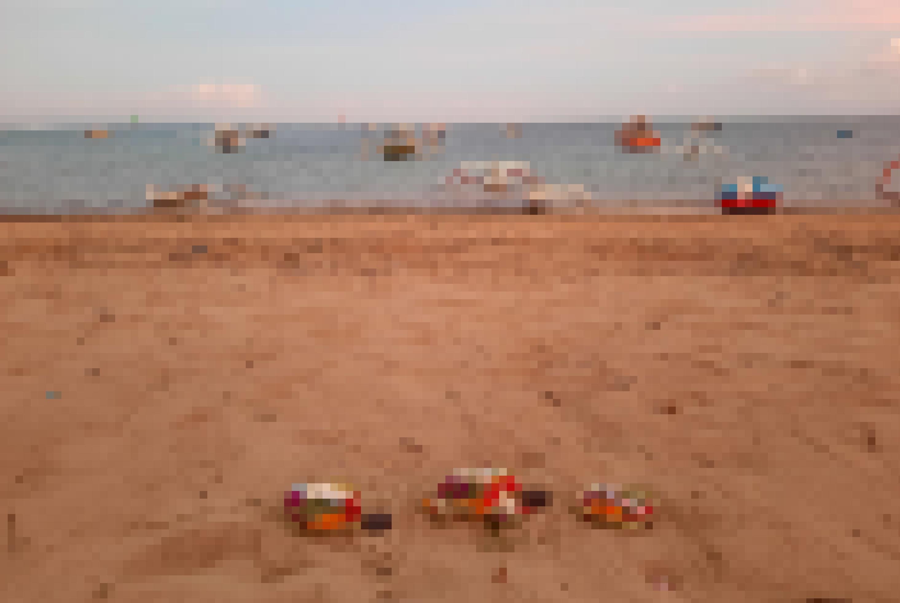 Am leeren Strand von Sanur liegen balinesische Opfergaben im Sand. Im Meer sind  Motorboote mit und ohne Ausleger zu sehen.