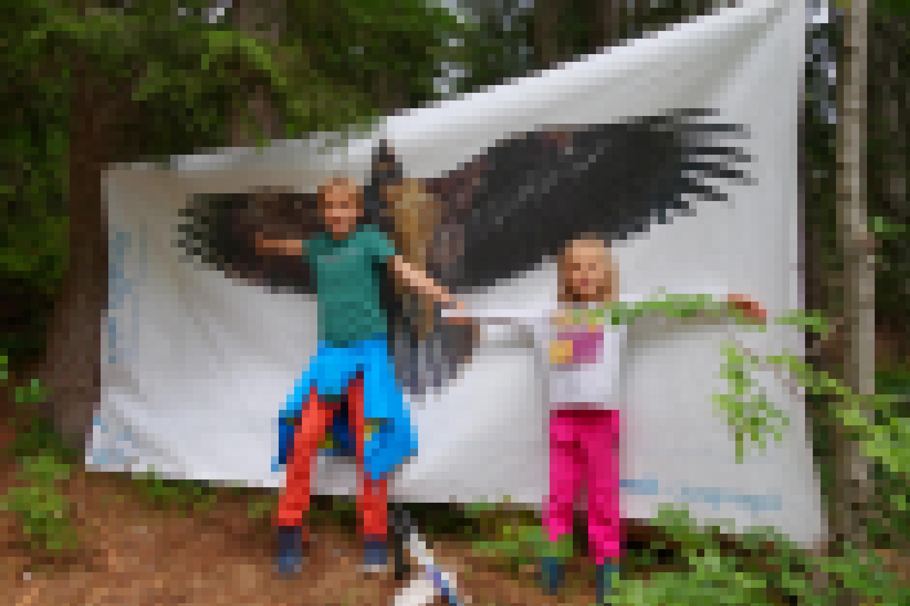 Ein Junge und ein Mädchen breiten ihre Arme vor einer lebensgroßen Abbildung eines fliegenden Bartgeiers aus.