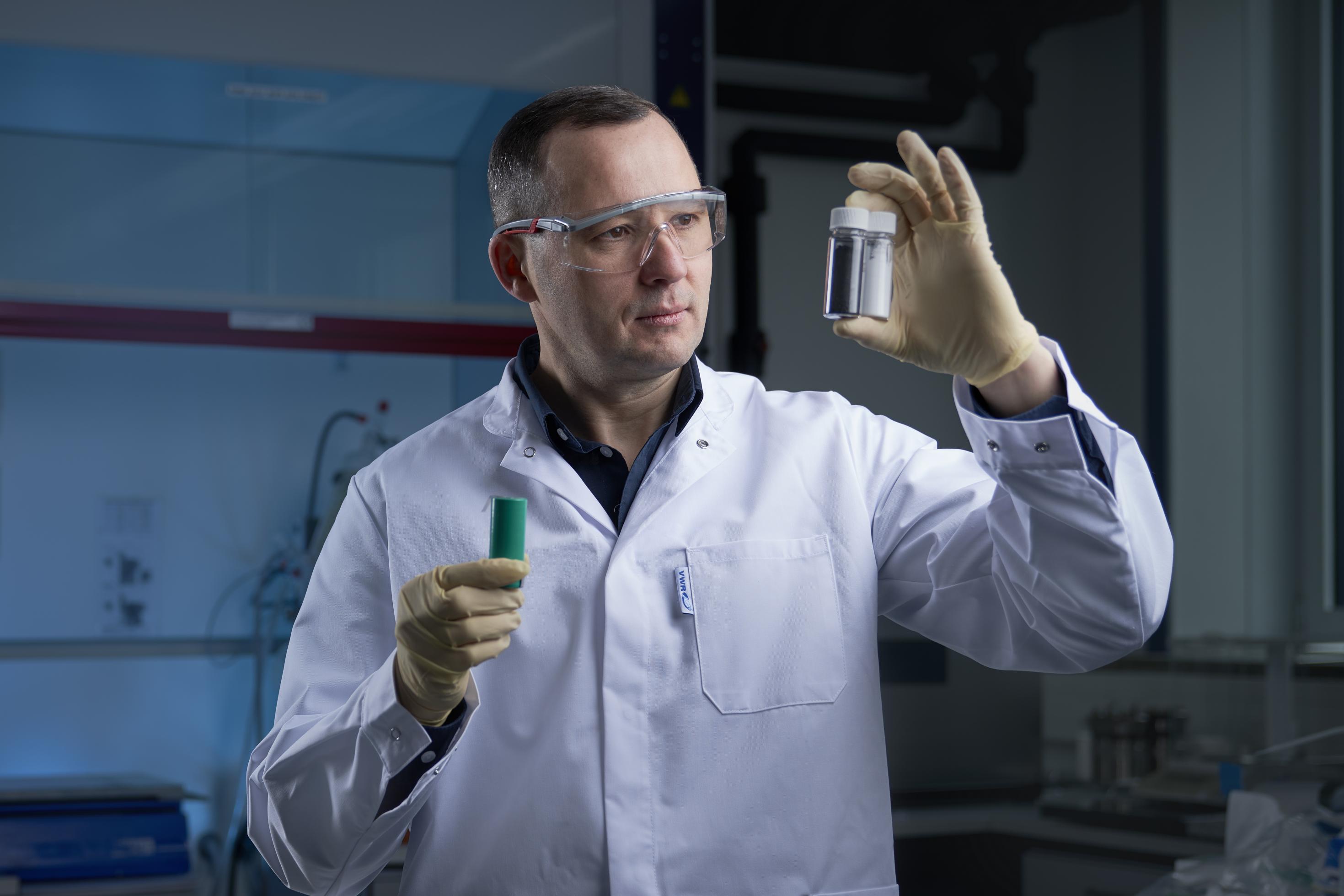 Dr. Oleksandr Dolotko, bekleidet mit Schutzbrille und Laborkittel, hält Probenröhrchen in die Luft.
