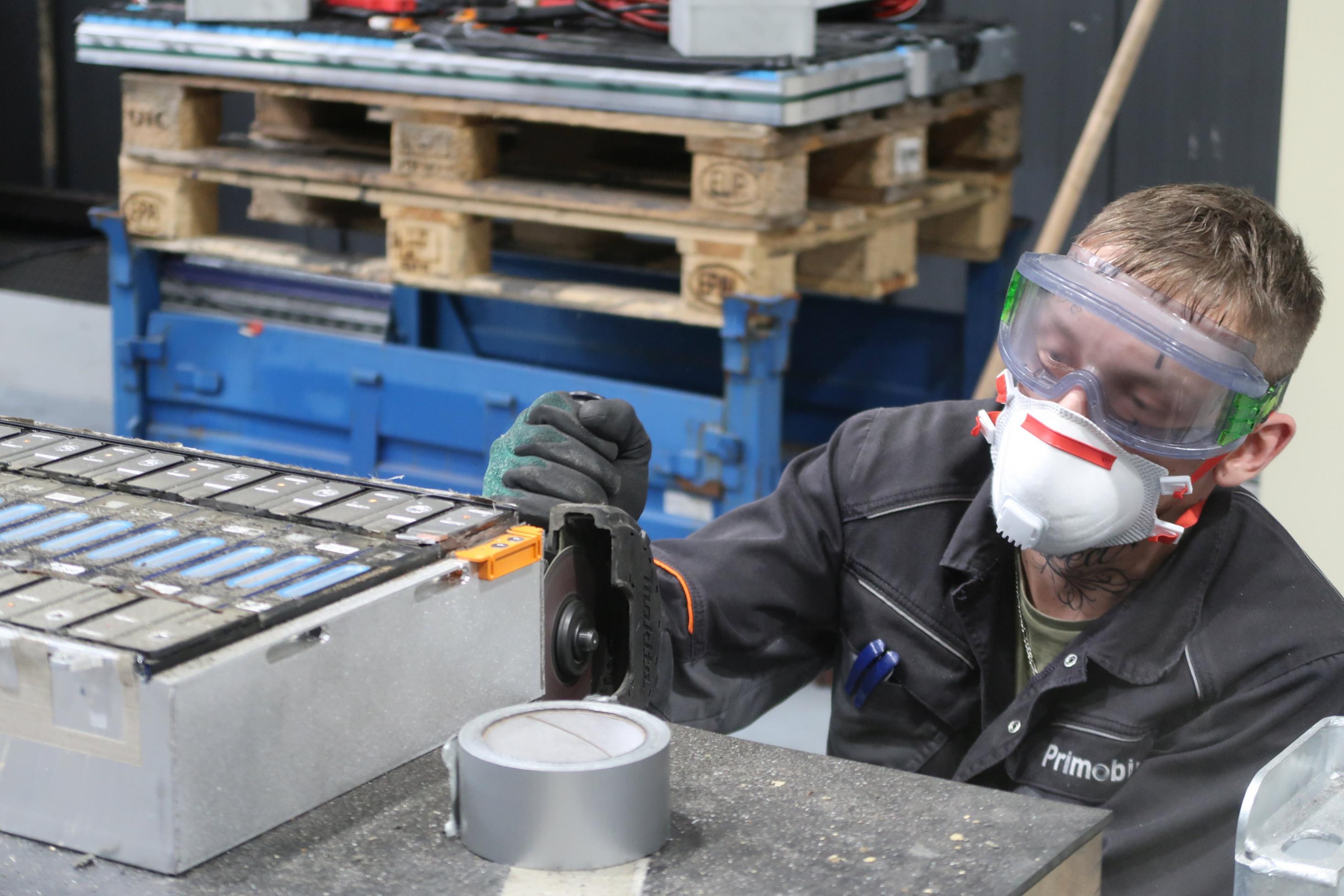Ein Mitarbeiter mit Schutzbrille und Schutzmaske schleift Batteriemodule mit einer Flex auf.
