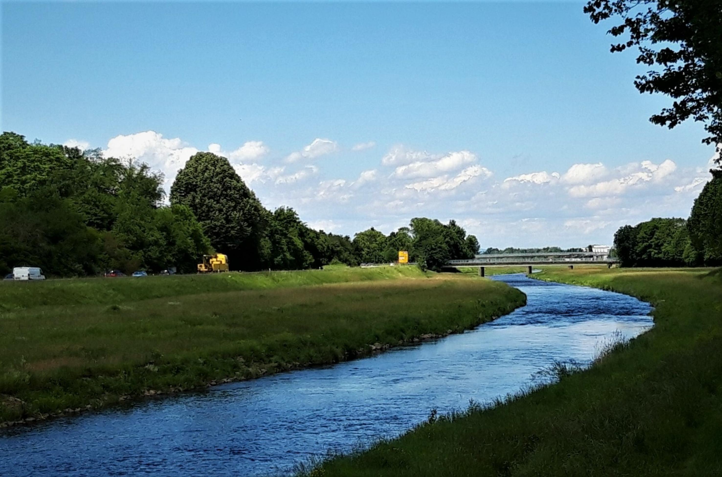 In fast giftig wirkendem Blau strahlt das Wasser der Murg normbreit zwischen den grünen Matten des zur Hochwasser-Bannung überbreiten, geradlinigen Flussbetts.