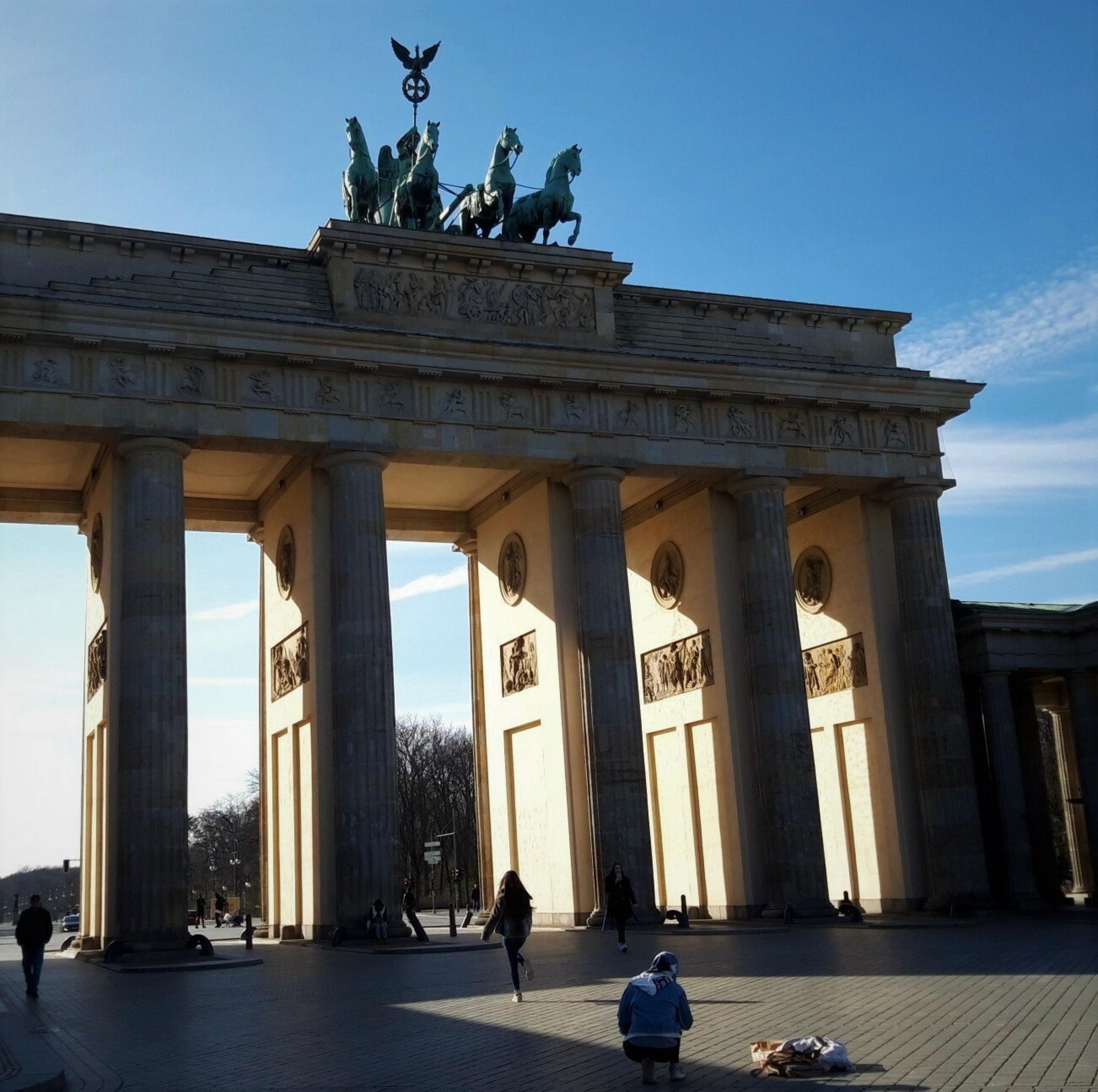 Seltene Leere vor dem Brandenburger Tor, durch das von Westen die Sonne scheint: Auf dem Vorplatz sind lediglich drei Passant·inn·en zu sehen.