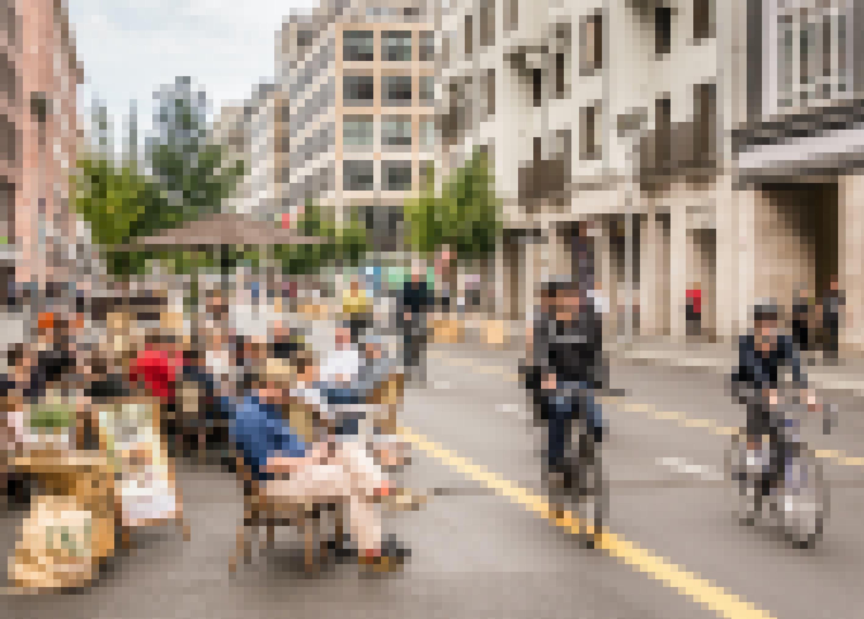 Am Straßenrand sitzen Menschen in einem Café. Radfahrer sind auf der Fahrbahn unterwegs, die für Autos gesperrt ist