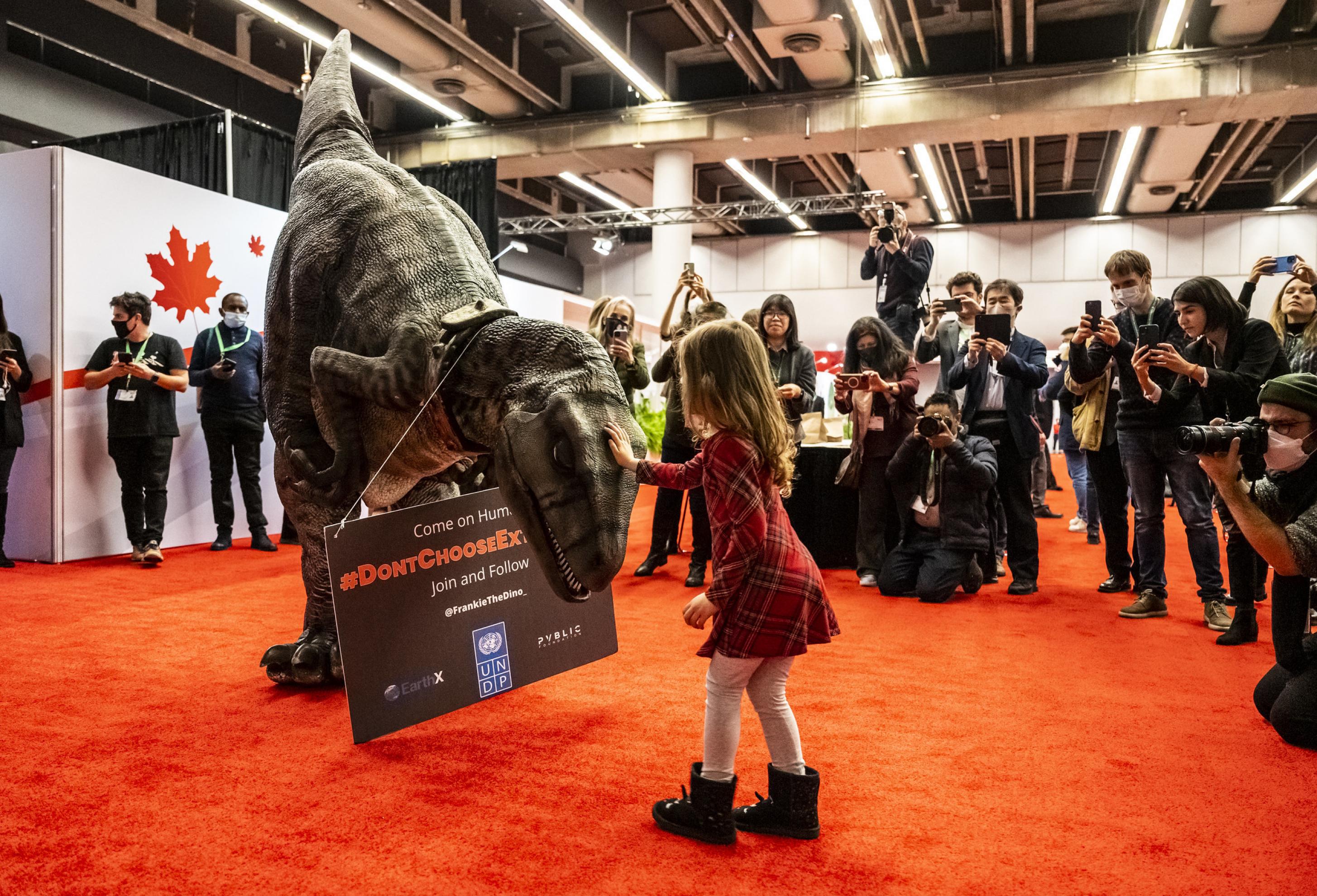 Ein Kind streichelt umringt von Fotografen einen Plastik-Dinosaurier.