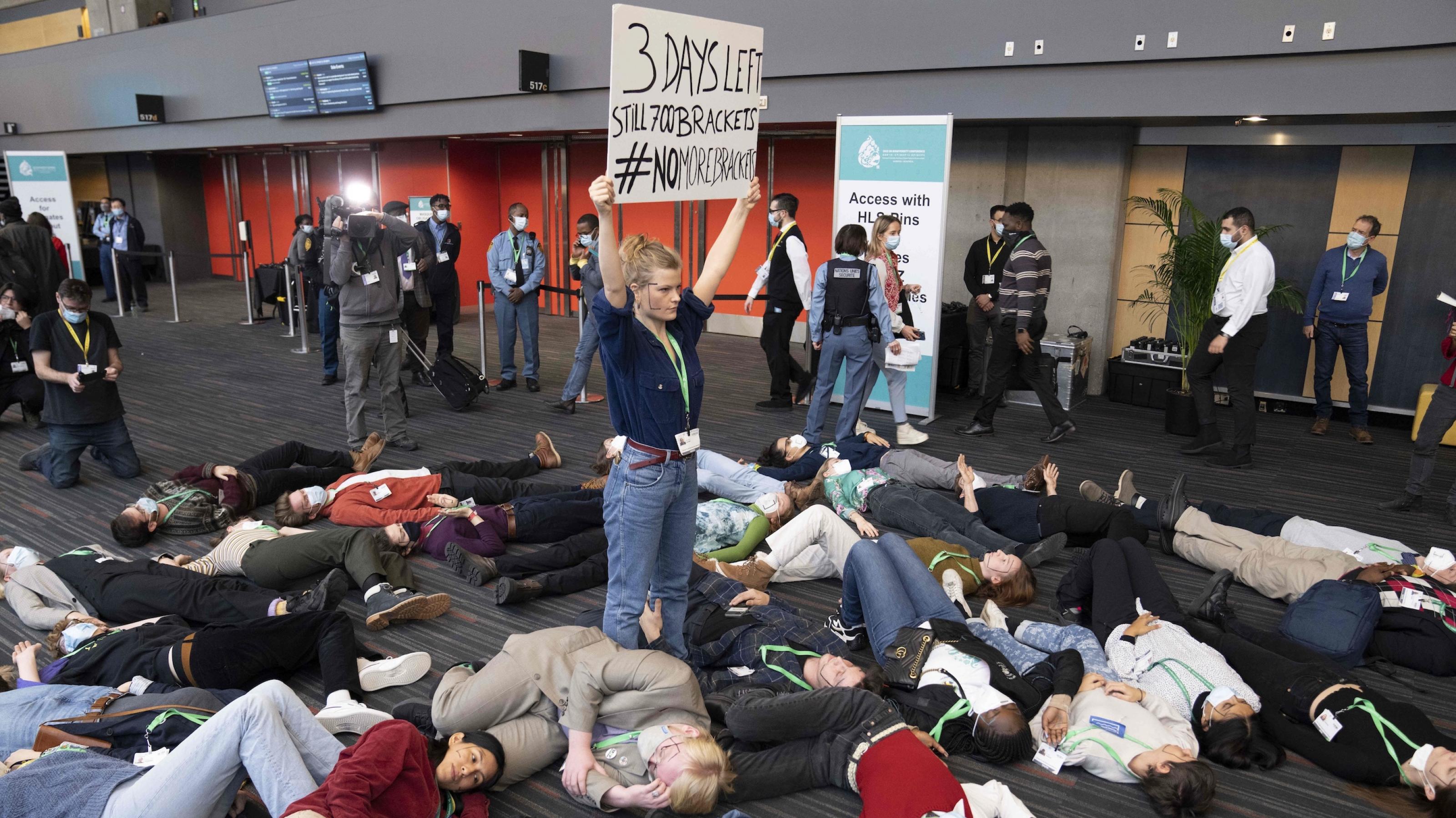 Junge Menschen liegen wie tot auf dem Boden des Konferenzzentrums, in der Mitte hält eine junge Frau ein Plakat hoch, auf dem „Noch 3 Tage“ steht.
