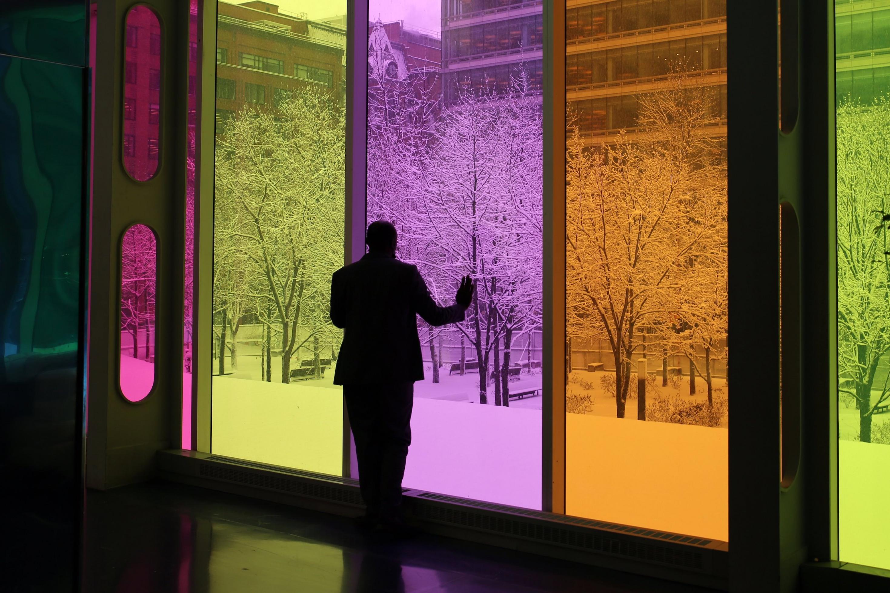 Mann steht an lilafarbenem Fenster, draußen liegt Schnee.