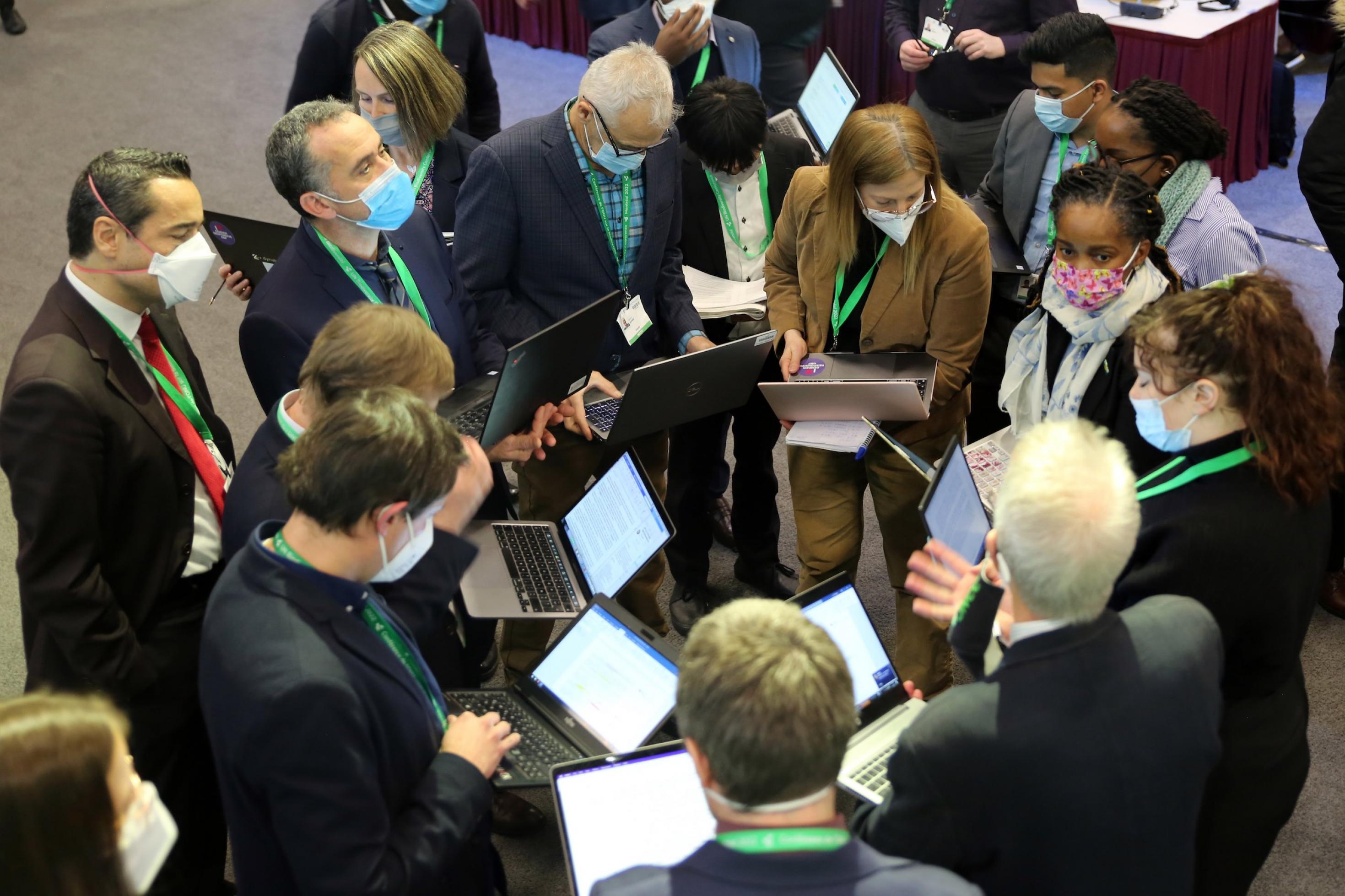 Menschen stehen mit ihren Laptops im Kreis in einer Konferenzhalle.