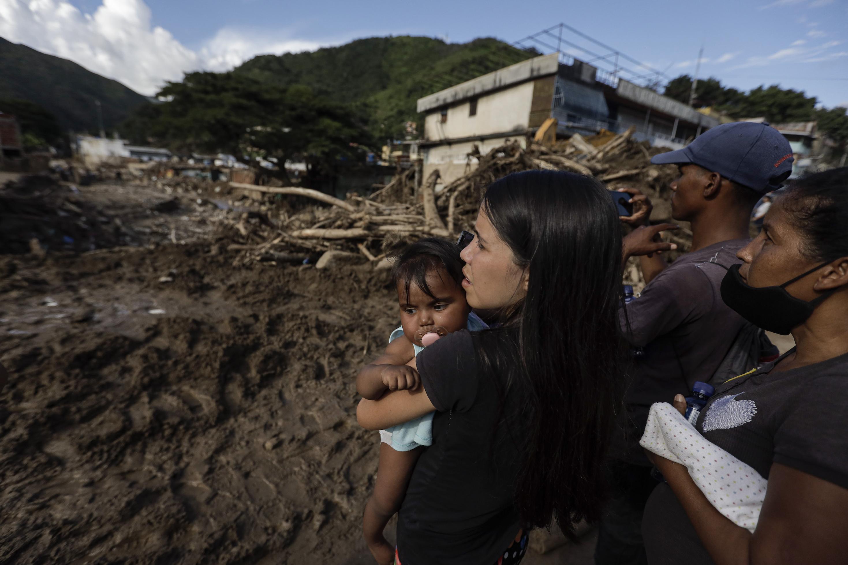 Eine Frau betrachtet mit ihrer Tochter und mehreren Nachbarn Schäden nach Überschwemmungen und einem Erdrutsch.