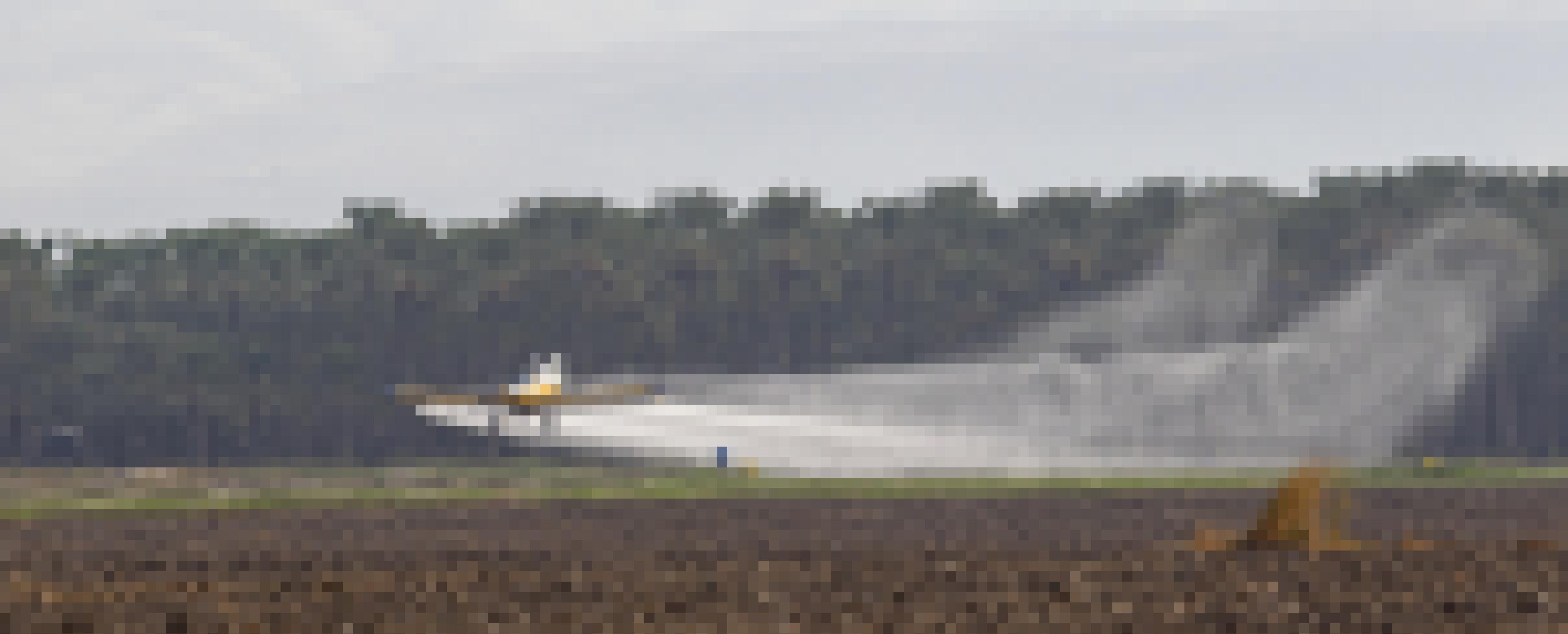 Ein Flugzeug verteilt im niedrigen Flug über ein Feld Chemikalien aus seinen Düsen. Im Hintergrund ein Palmenhain