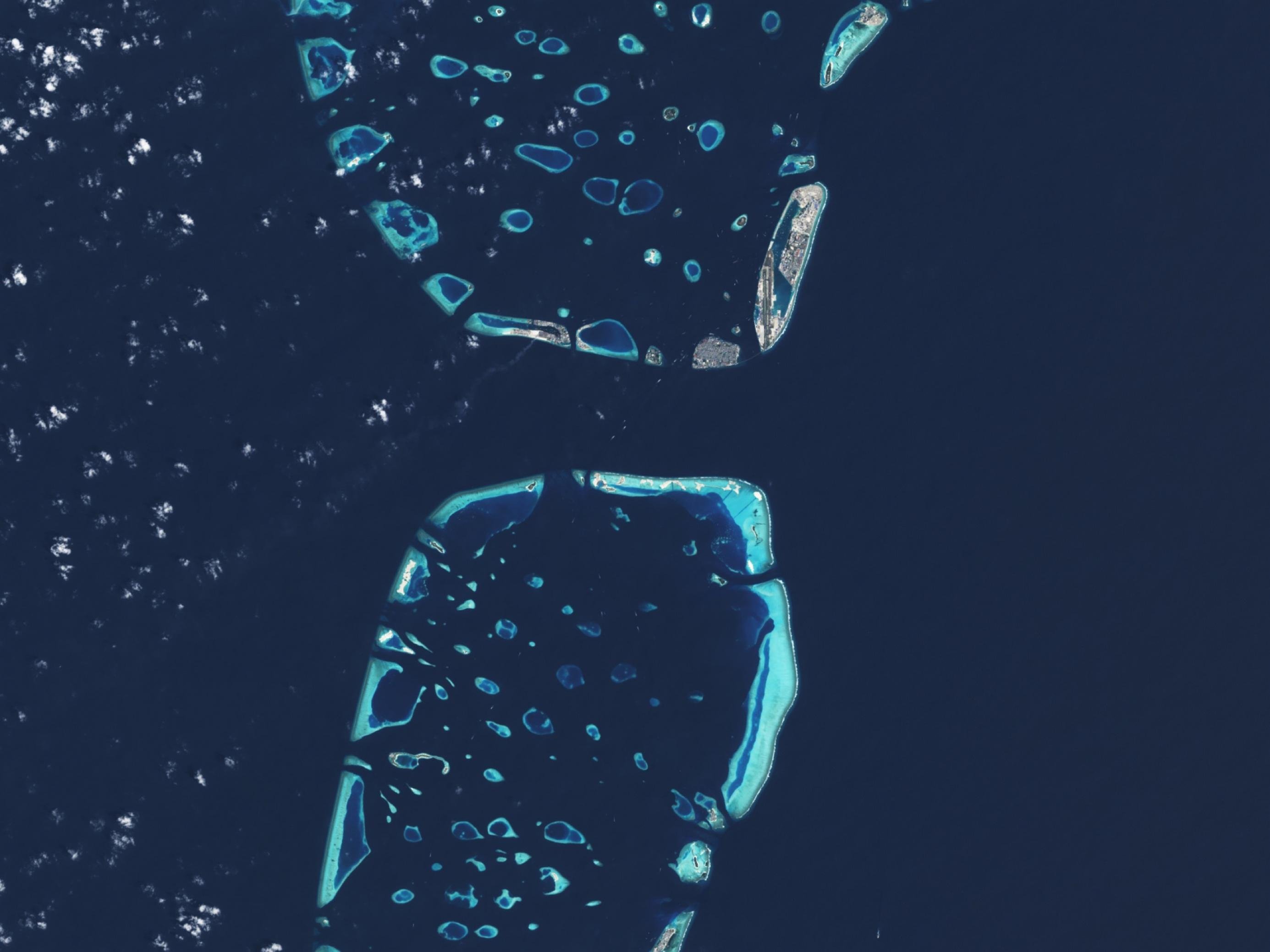 Satellitenaufnahme zeigt Koralleninseln im Indischen Ozean und die bebaute Hauptinsel der Malediven aus großer Höhe.