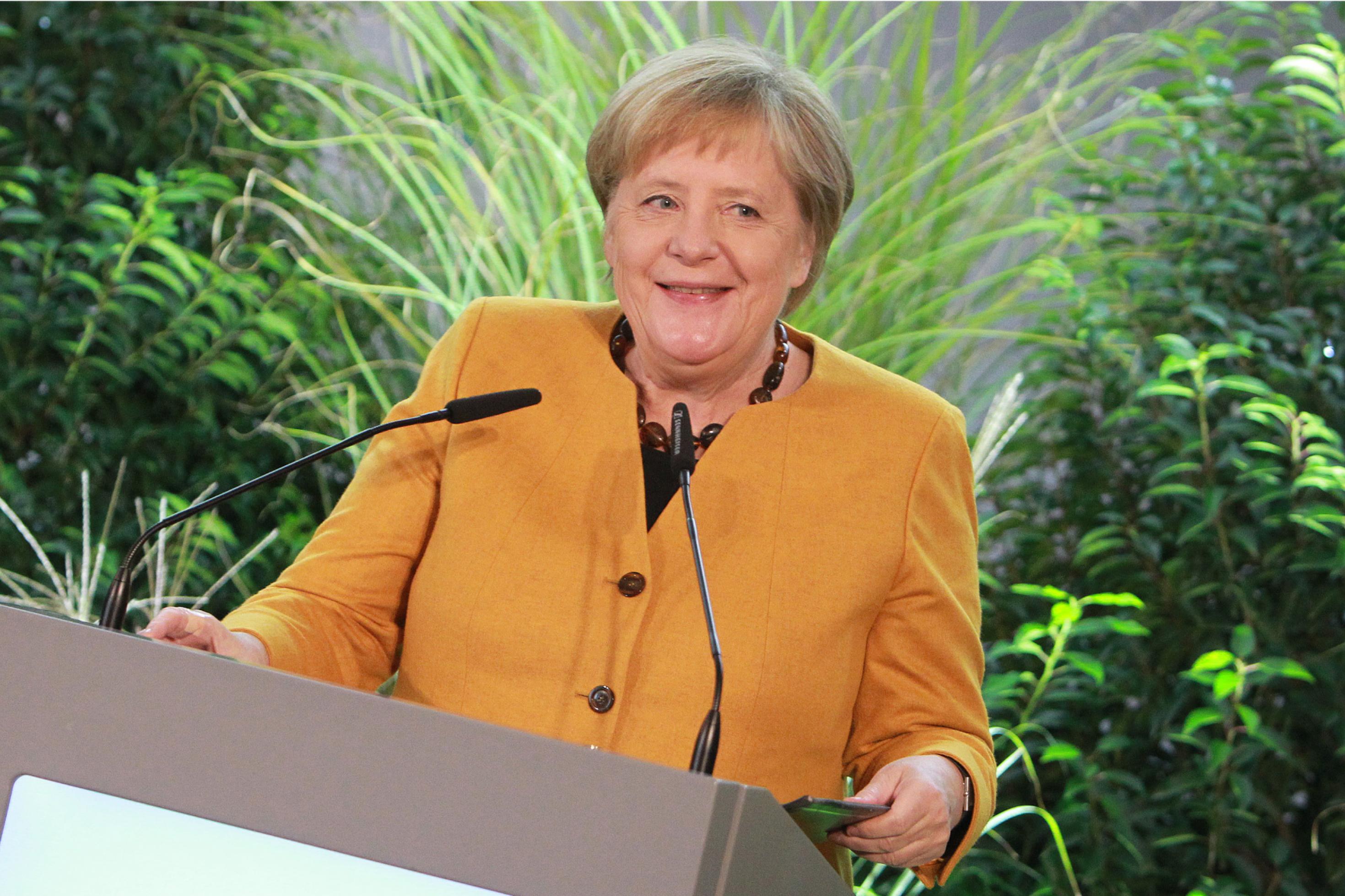 Bundeskanzlerin Angela Merkel hinter einem Rednerpult. Im Hintergrund grüne Pflanzen.