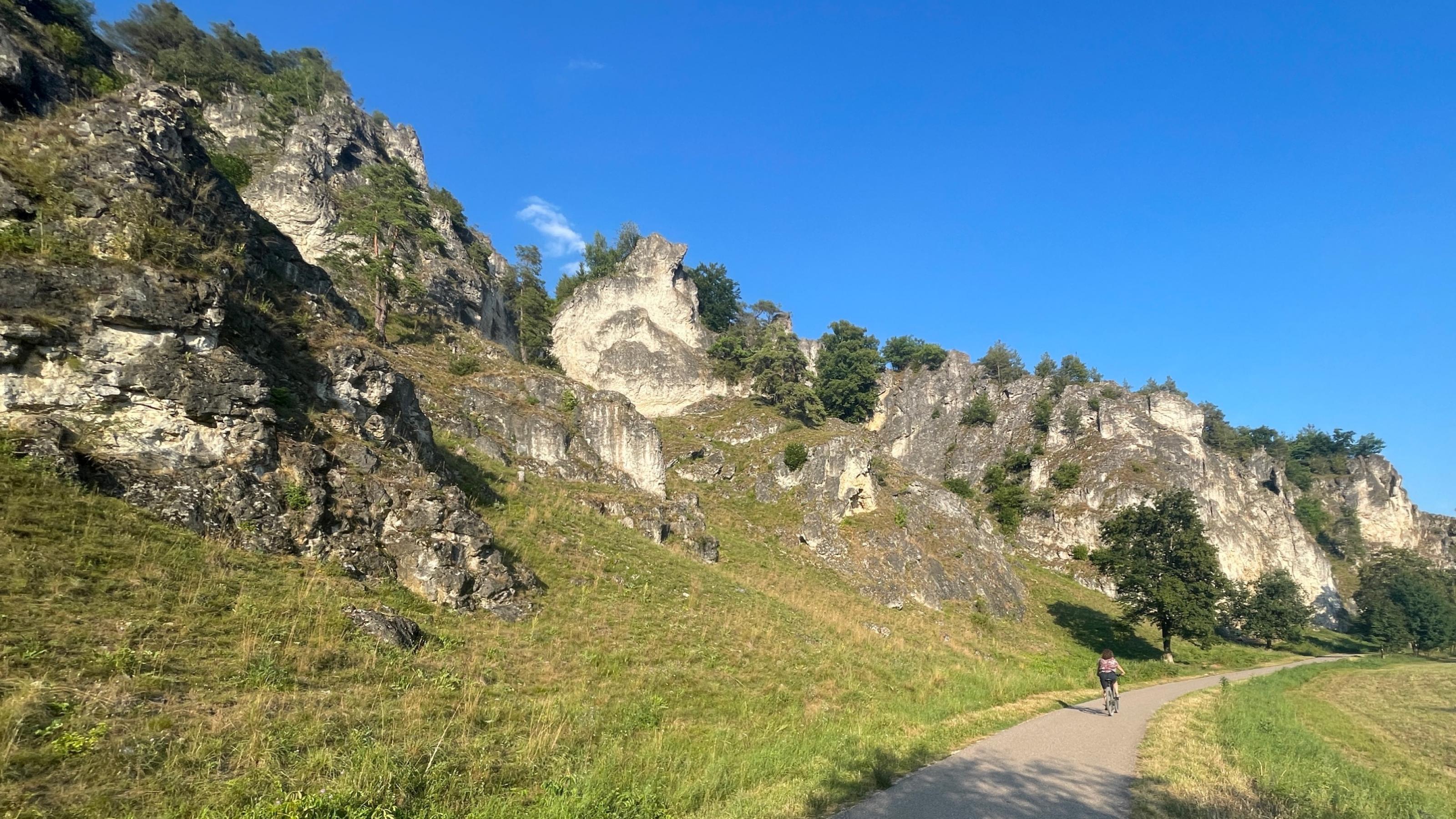 Karstige Felsen mit Trockenrasen entlang eines Radwegs.