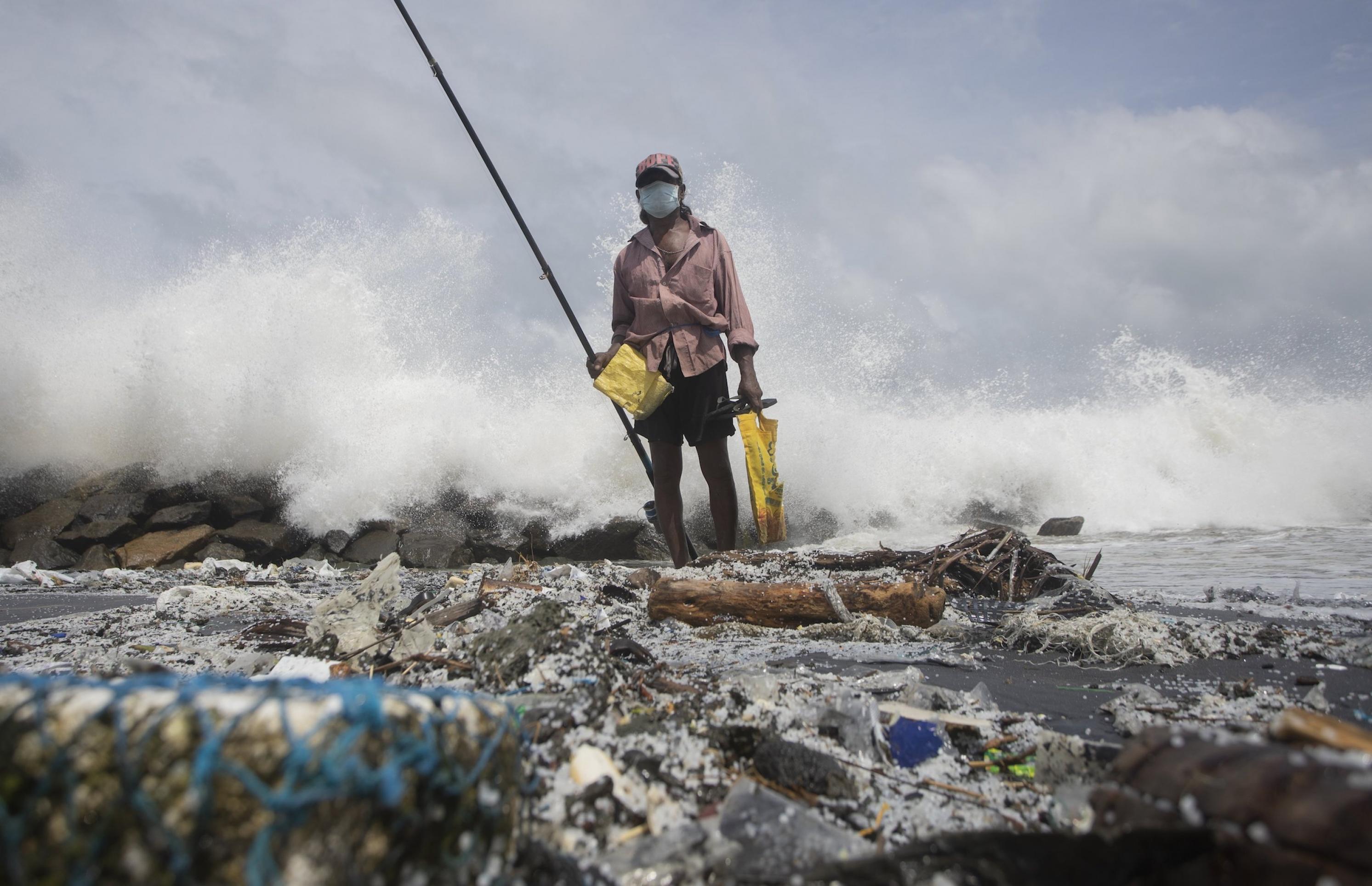 Mann steht an plastikverseuchter Küste mit Angel.