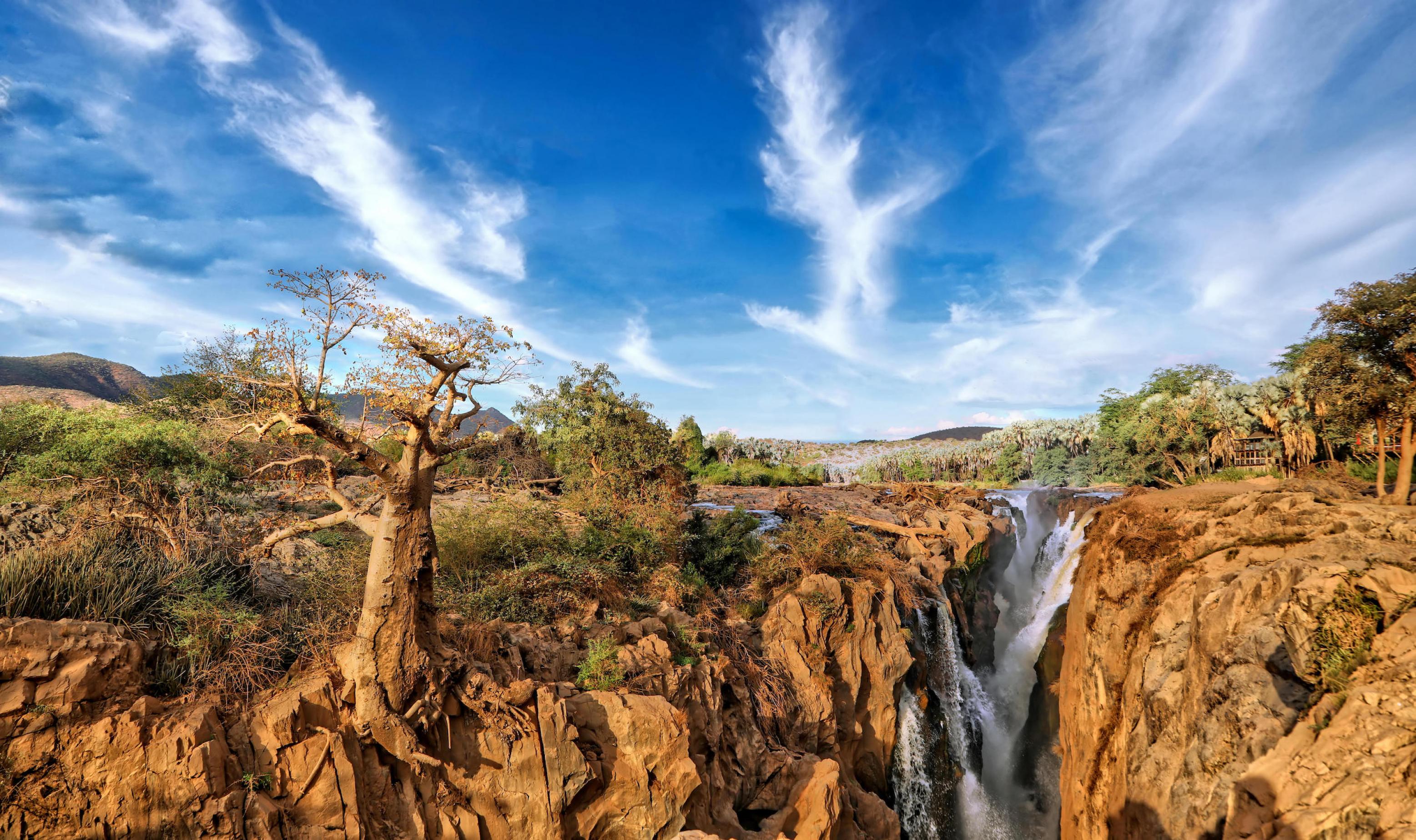 Wasserfall in einer wilden, trockenen Landschaft, am Rand ein großer Baum.