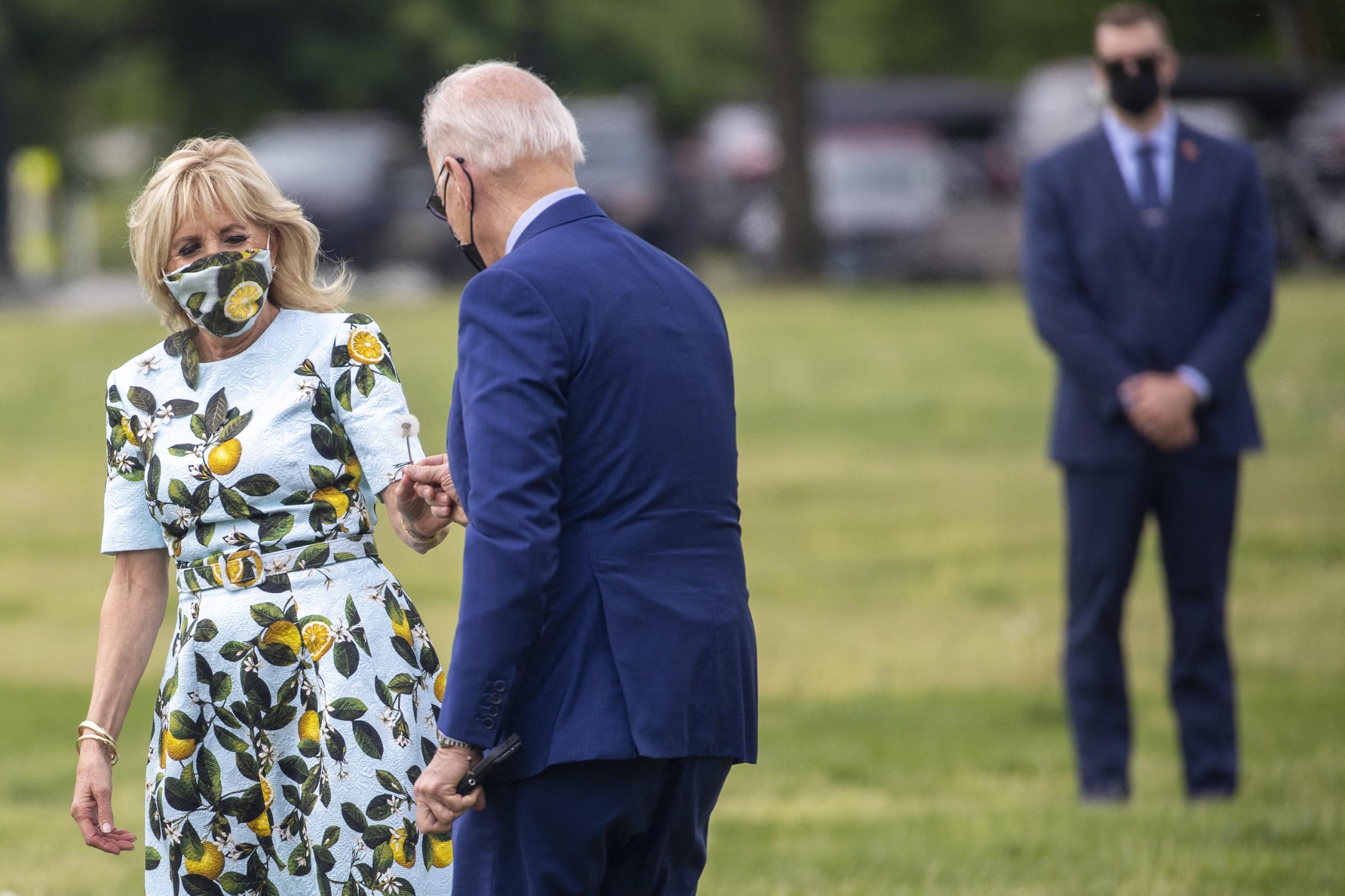 US-Präsident Joe Biden reicht seiner Frau eine Löwenzahnpflanze, die er für sie gepflückt hat. Jill Bidens Kleid ist mit Blättern und Zitronen bedruckt.