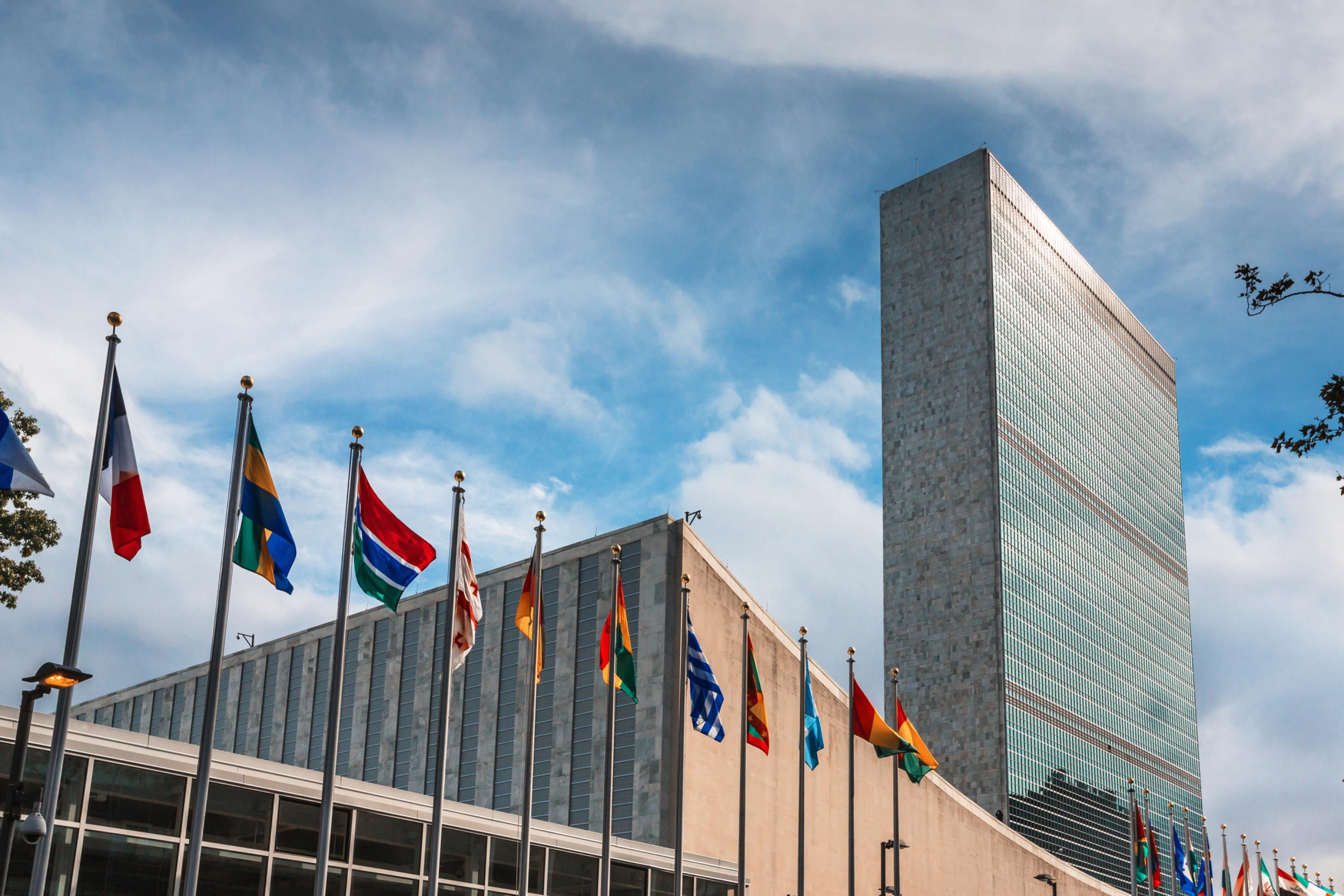 Außenaufnahme des Hochhauses der Vereinten Nationen in New York mit zahlreichen Flaggen von Mitgliedsstaaten.