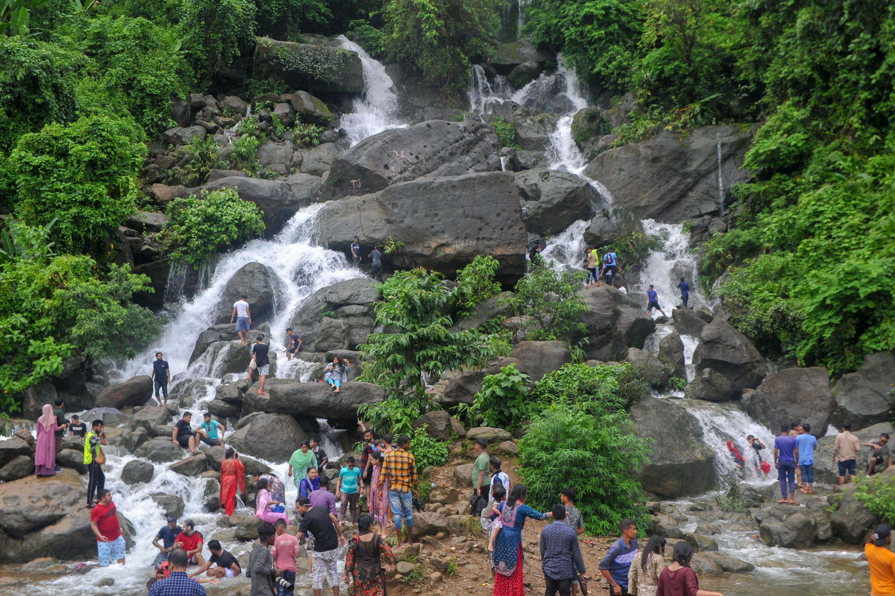 Menschen stehen in Bangladesch am Fuss eines großen Wasserfalls, der aus dem Wald kommt.
