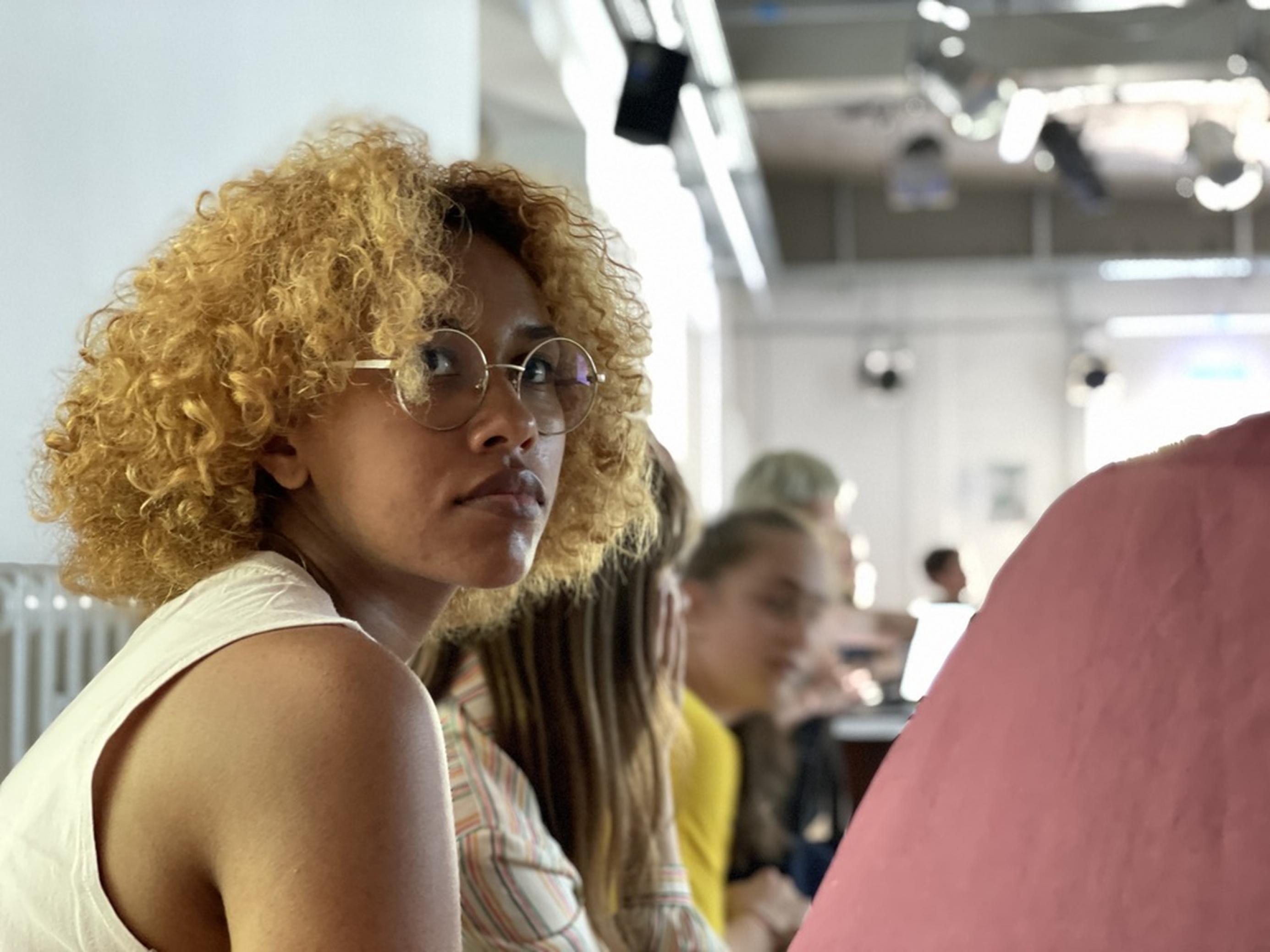 Das Porträt zeigt Alicia beim Zuhören, während ihre Kollegïnnen einen interaktiven Theater-Workshop gestalten.