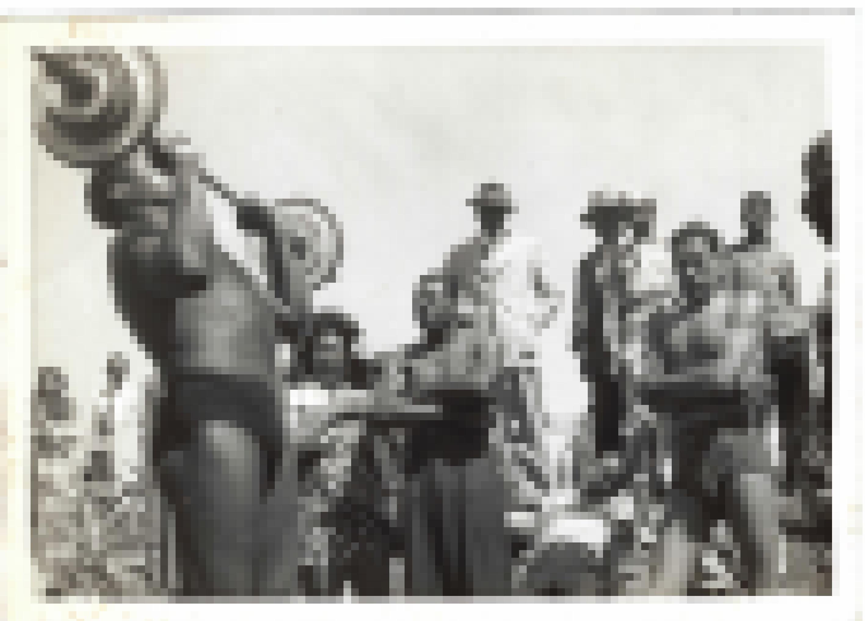 Ein Mann mit freiem Oberkörper und Badehose stemmt eine Hantel vor Freunden und Neugierigen, manche in Sommerkleidern, andere ebenfalls in Schwimmkleidung. Alle sind Schwarz. Aufgenommen ca. 1945–1950