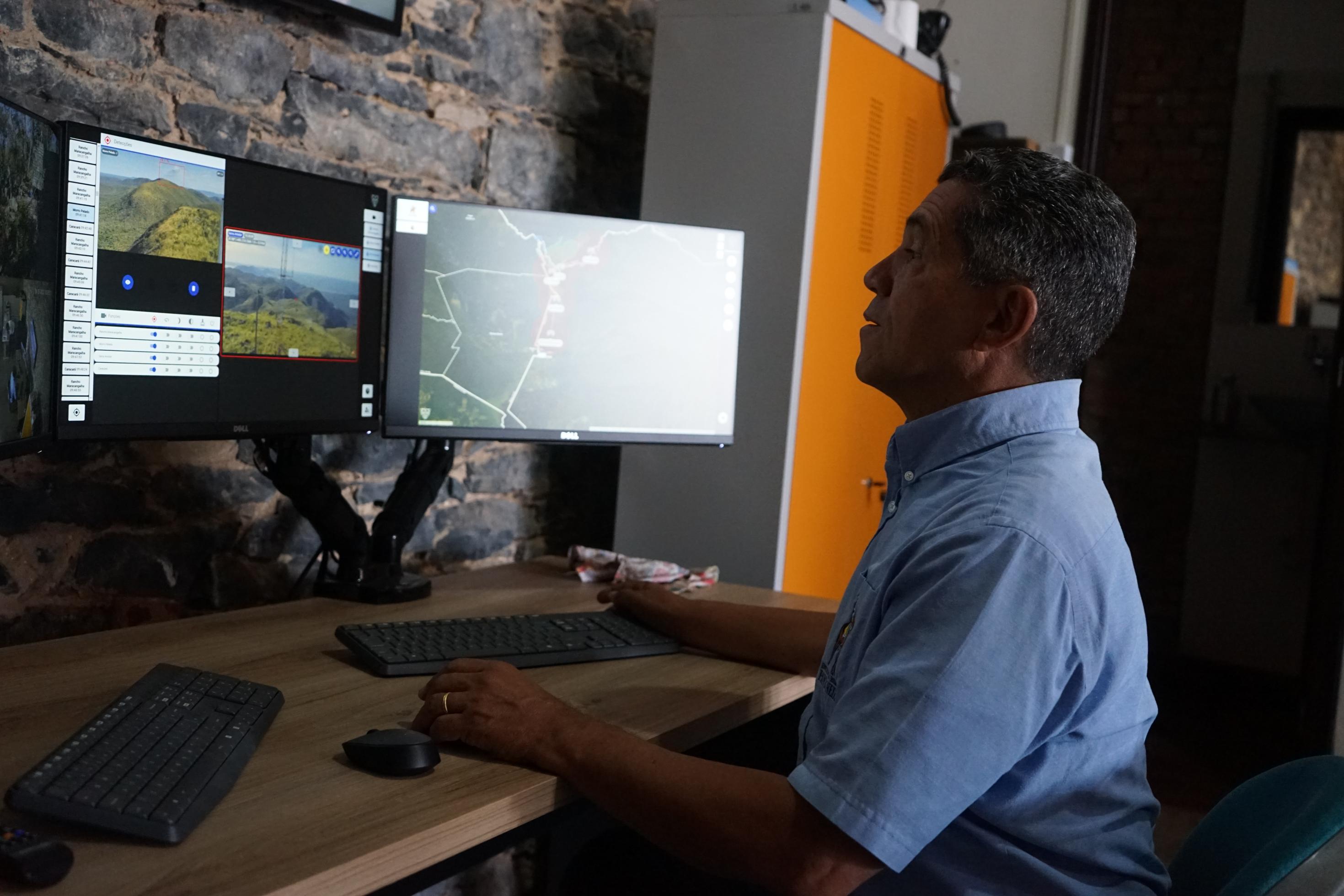 Ein grauhaariger Mann blickt auf mehrere Computerbildschirme vor ihm.