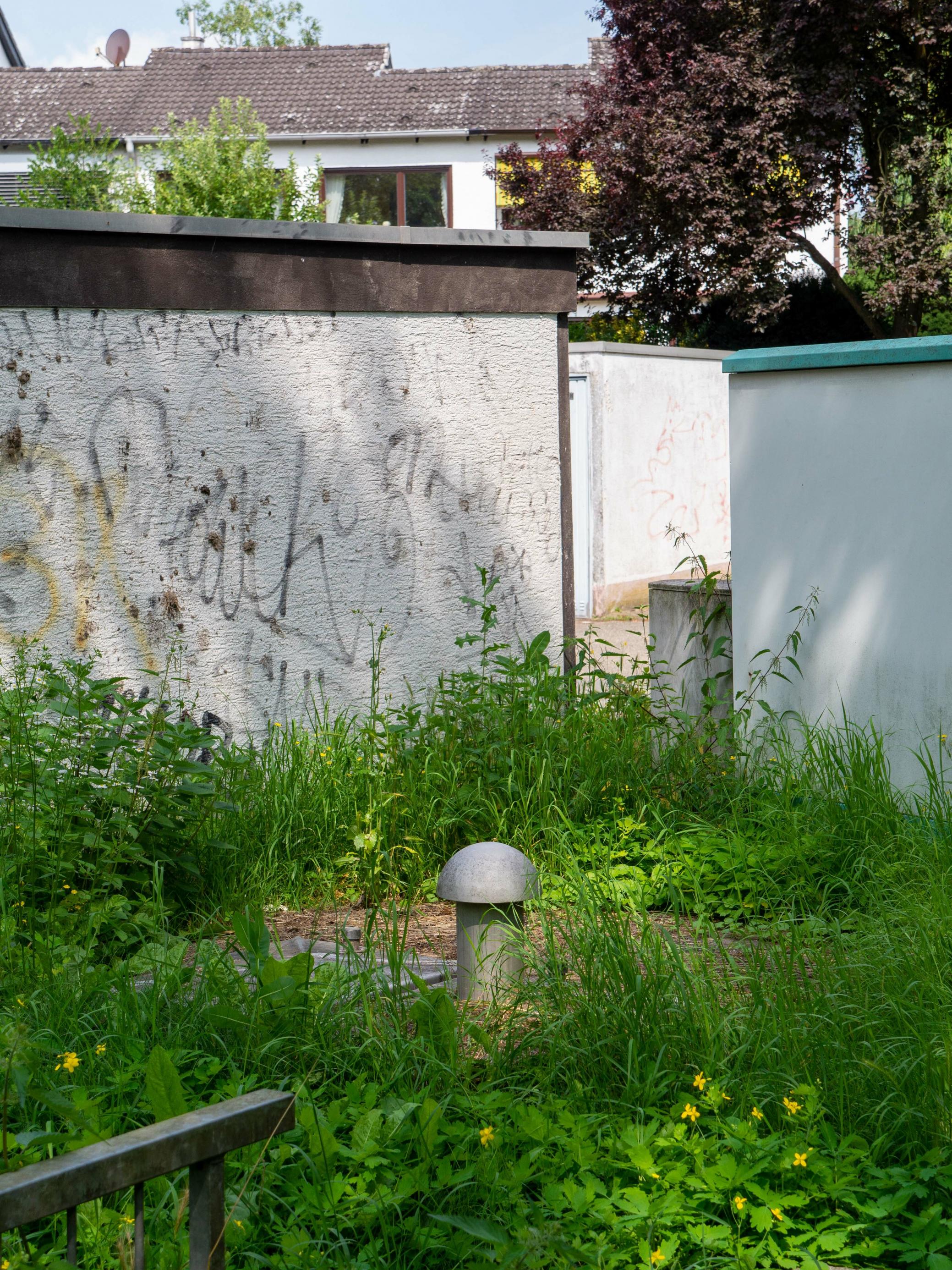 Am pilzförmigen Belüftungsstutzen ist einer der Brunnen hinter Garagenwänden zu erkennen, im Hintergrund Wohnhäuser
