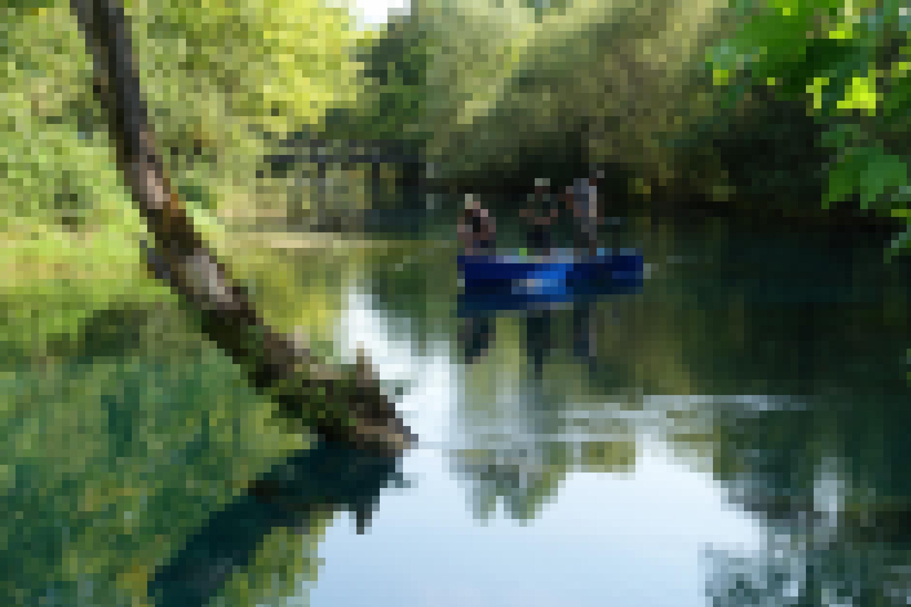 Fluss mit Bäumen, kleines Boot, darin Fischer, im Hintergrund eine Holzbrücke
