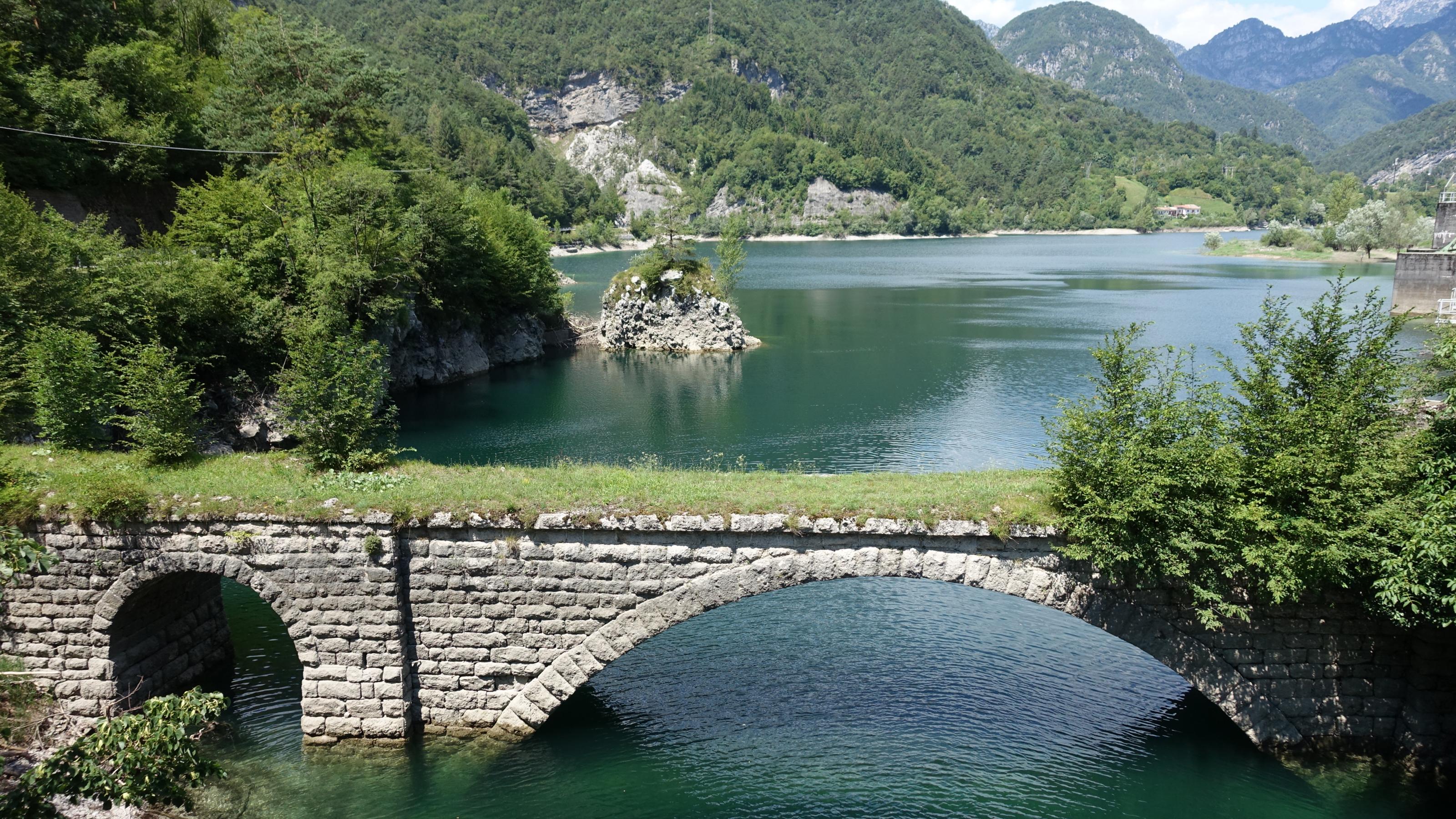 Stausee des Flusses Meduna, dahinter schroffe Berge mit Wald, vorne eine alte Steinbrücke