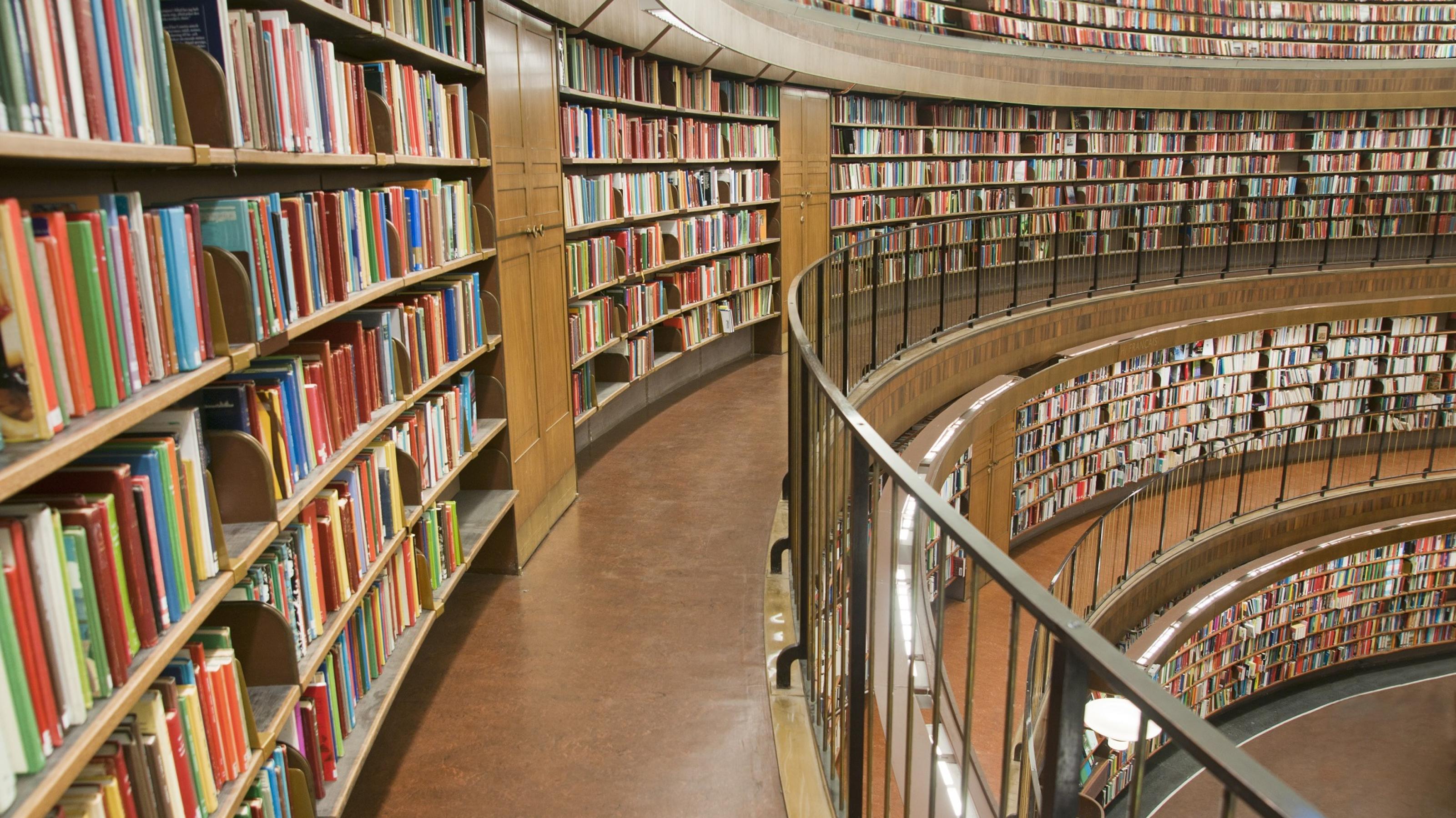 Eine Bücherei, die mehrstöckig aufgebaut ist, ein Gang geht zur Seite zur oberen rechten Ecke des Bildes