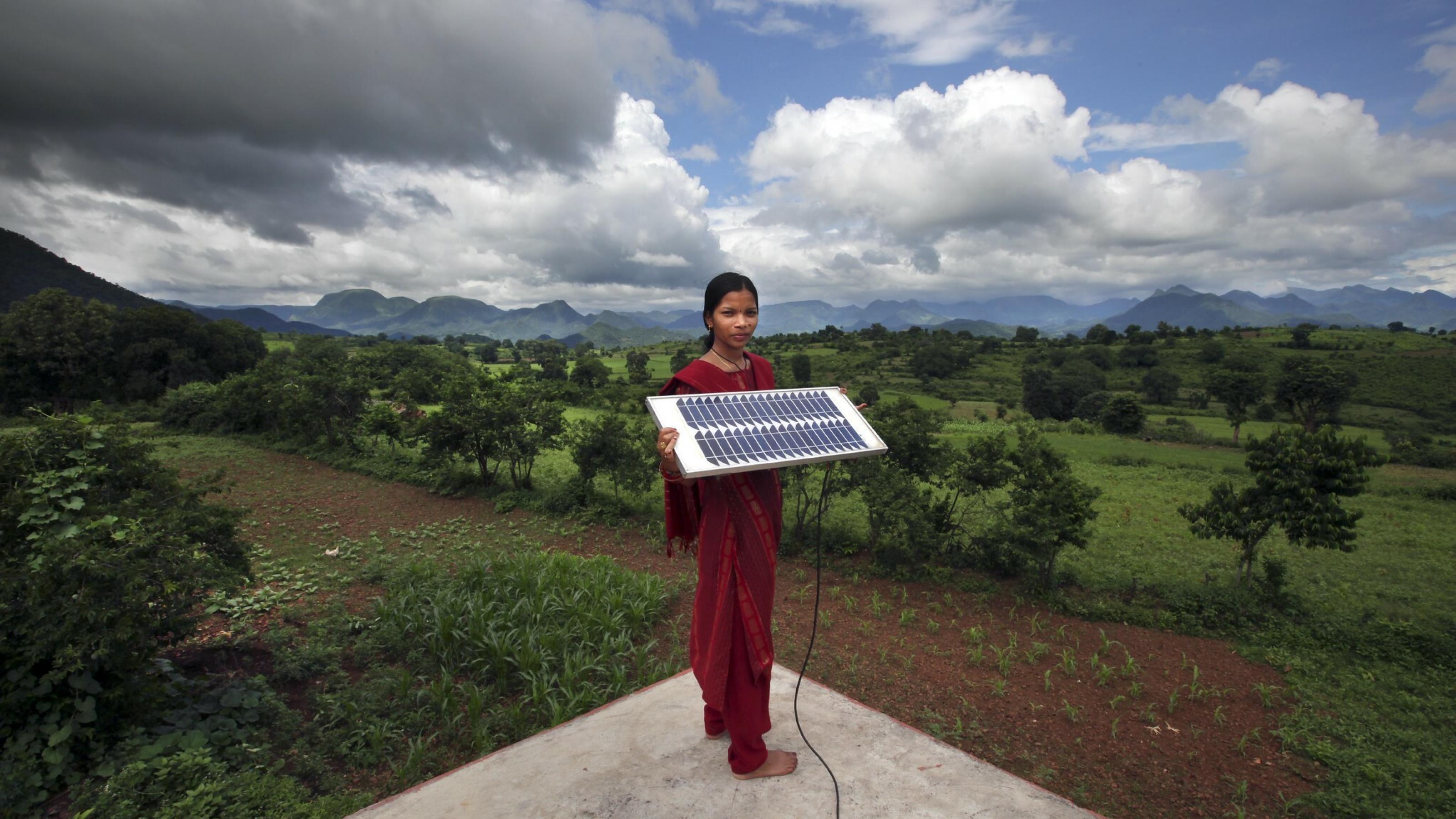 Ein barfüßige Solaringenieurin im Solarstromdorf Tinginapu in Indien steht auf dem Dach eines Hauses und hält ein Solarmodul in der Hand.