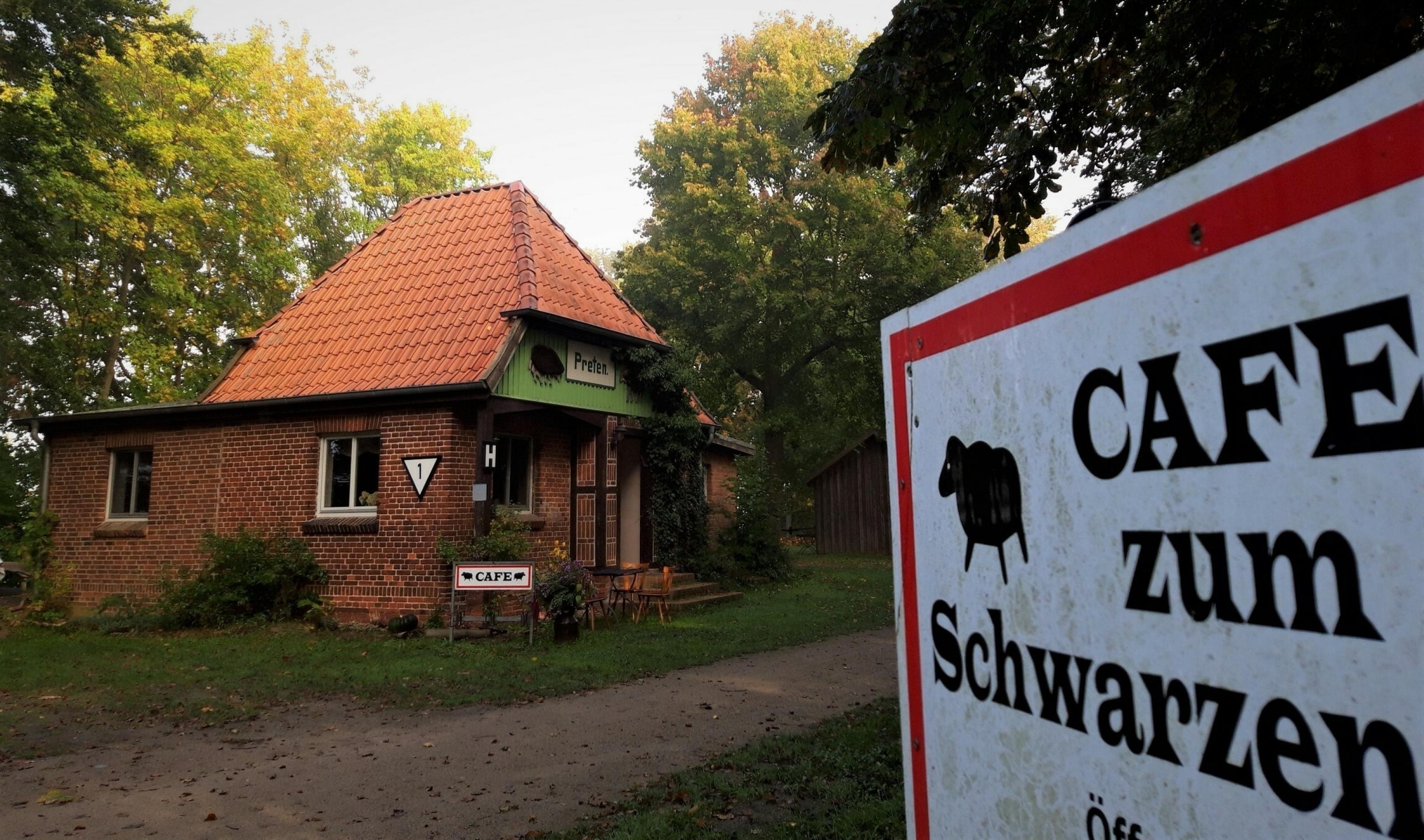 Hinter der schwarz-weiß-roten Werbetafel des „Cafe zum Schwarzen Schaf“ erhebt sich das einstige, kleine Bahnhofsgebäude, gemauert aus roten Klinkern und mit dem Originalschriftzug „Preten“.