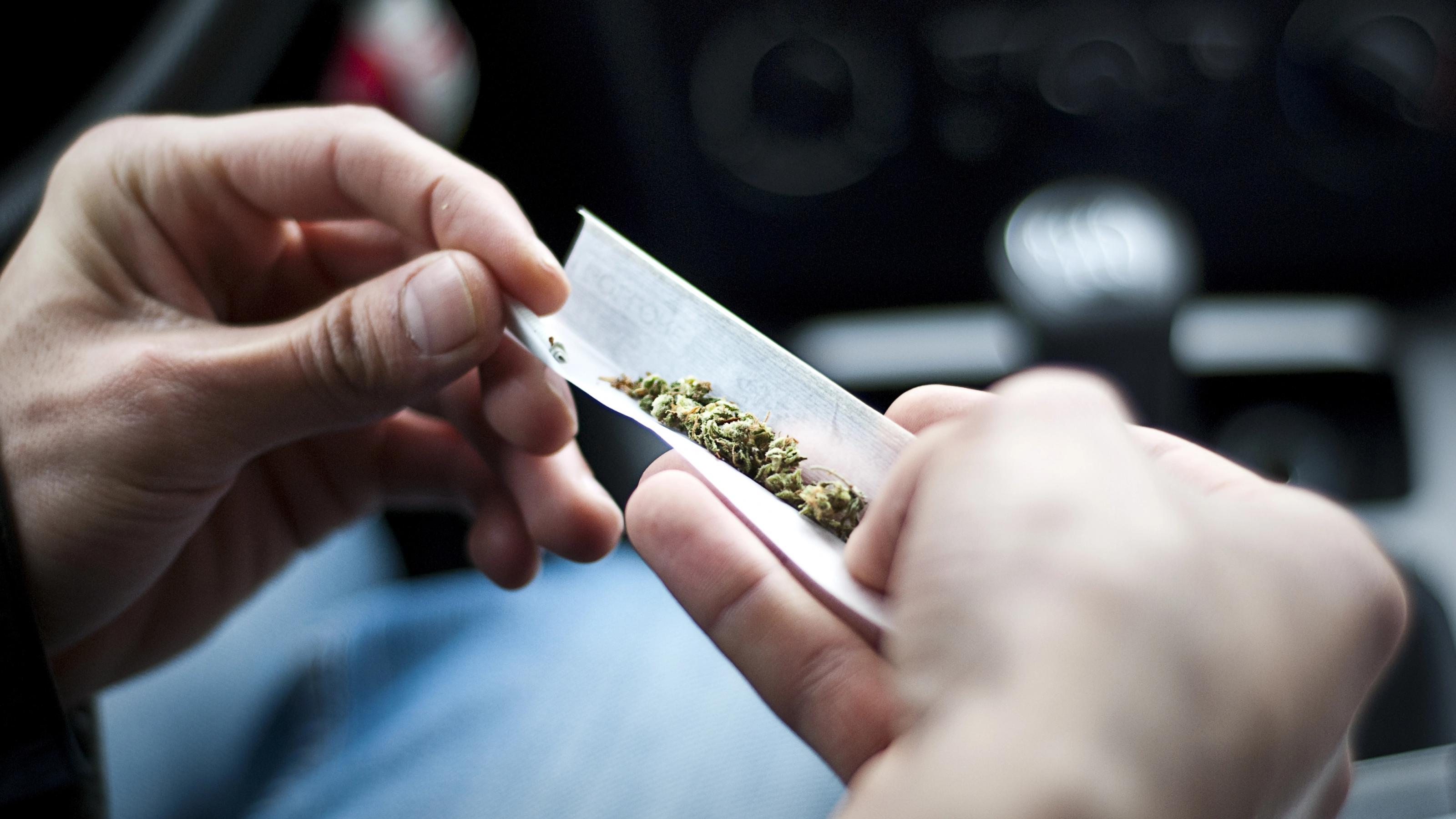 Das Foto zeigt zwei Hände, die ein ein Blättchen mit Cannabis/Gras halten, um einen Joint zu drehen.