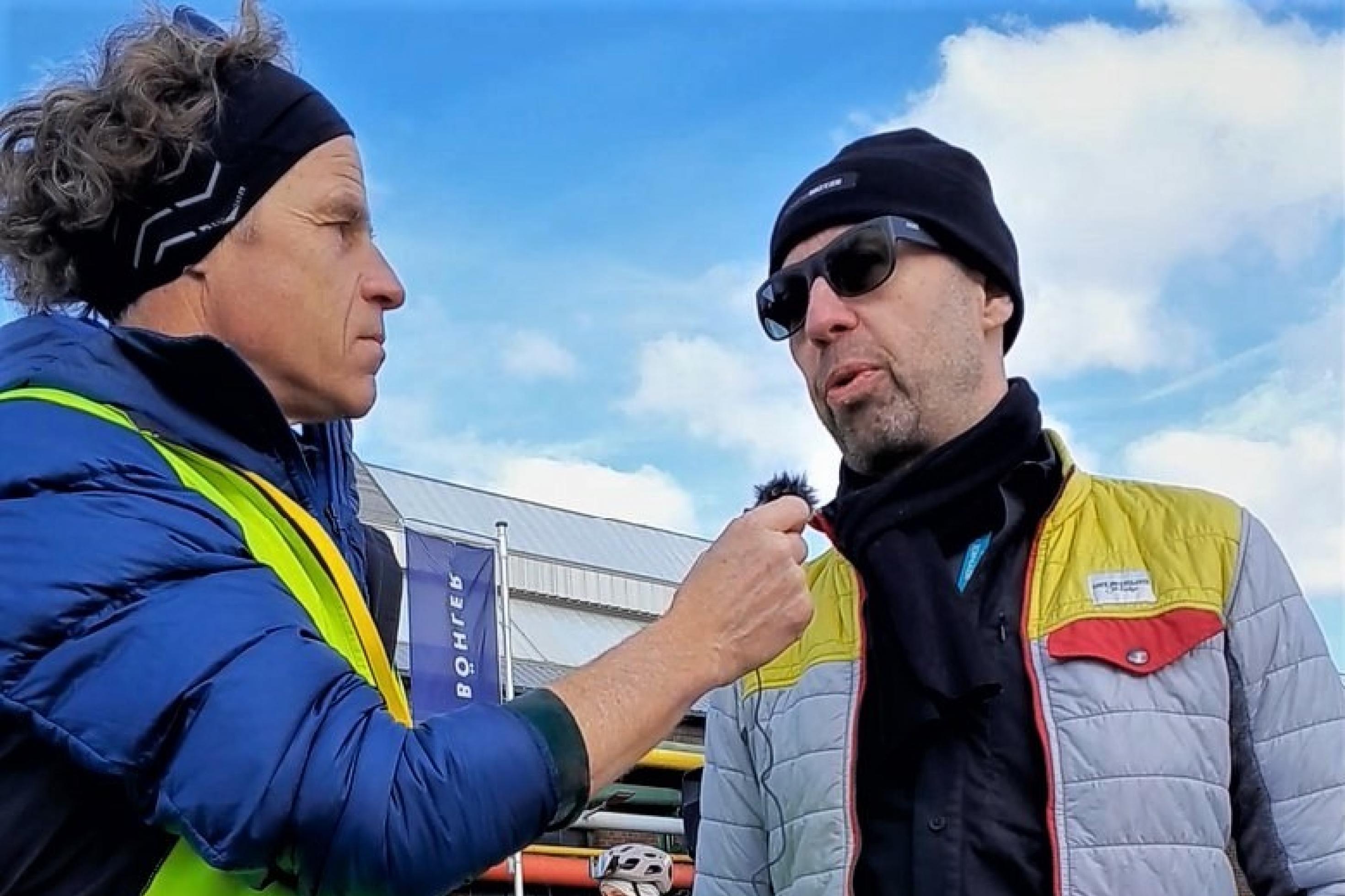 Der Reporter, links, hält dem sonnenbebrillten Radexperten unter freiem Himmel ein Mikrophon unter die Nase