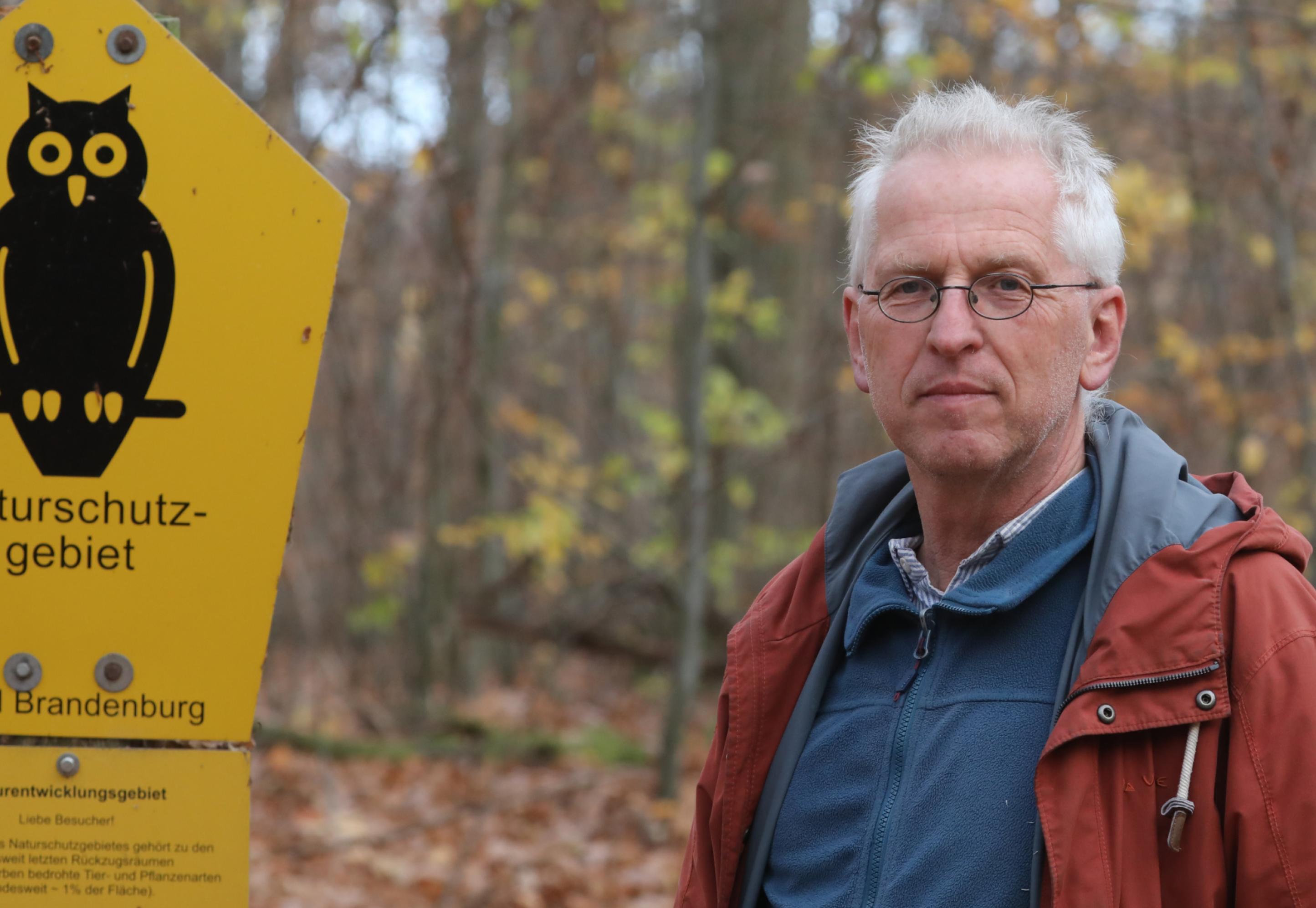 Martin Flade steht neben einem Naturschutzgebiet-Schild im Wald