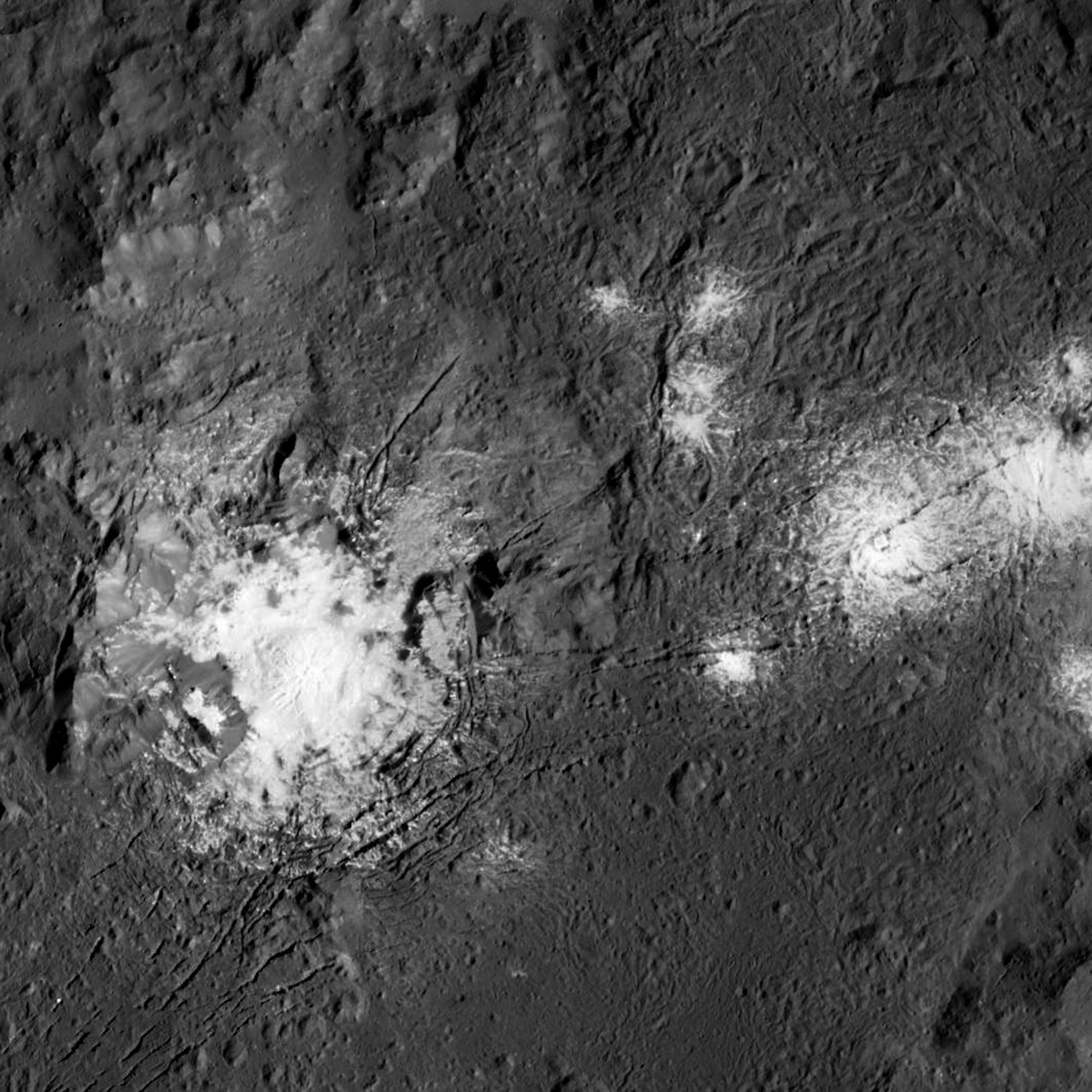 Ein großer Krater in grauer Landschaft, darinnen ist ein heller (überstrahlter) Fleck, rechts davon einige weitere Flecken, wie verplemperte Milch