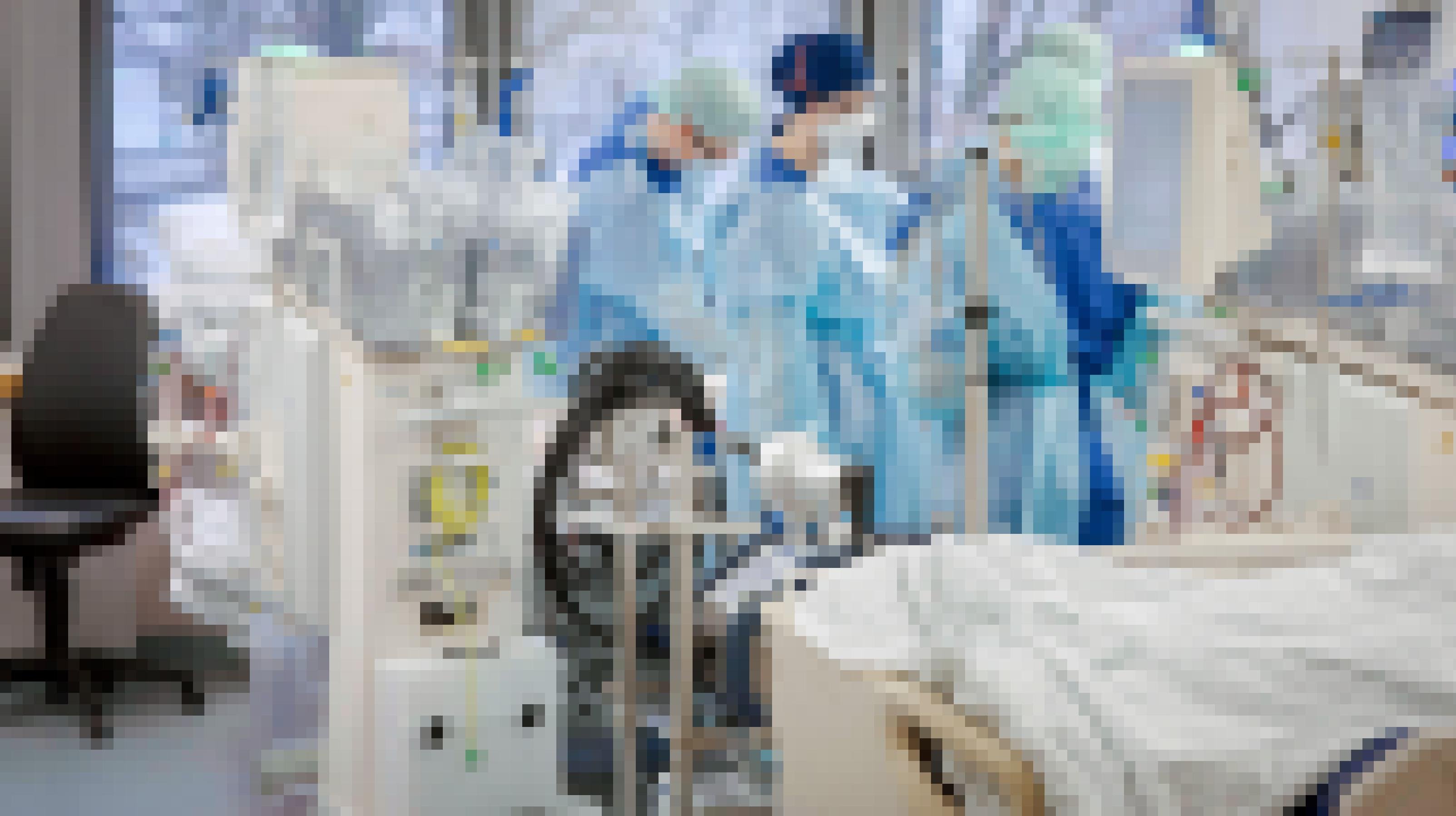 Intensivmedizinerïnnen bei der Arbeit – in Schutzkleidung in einem Krankenzimmer mit vielen medizinischen Geräten.