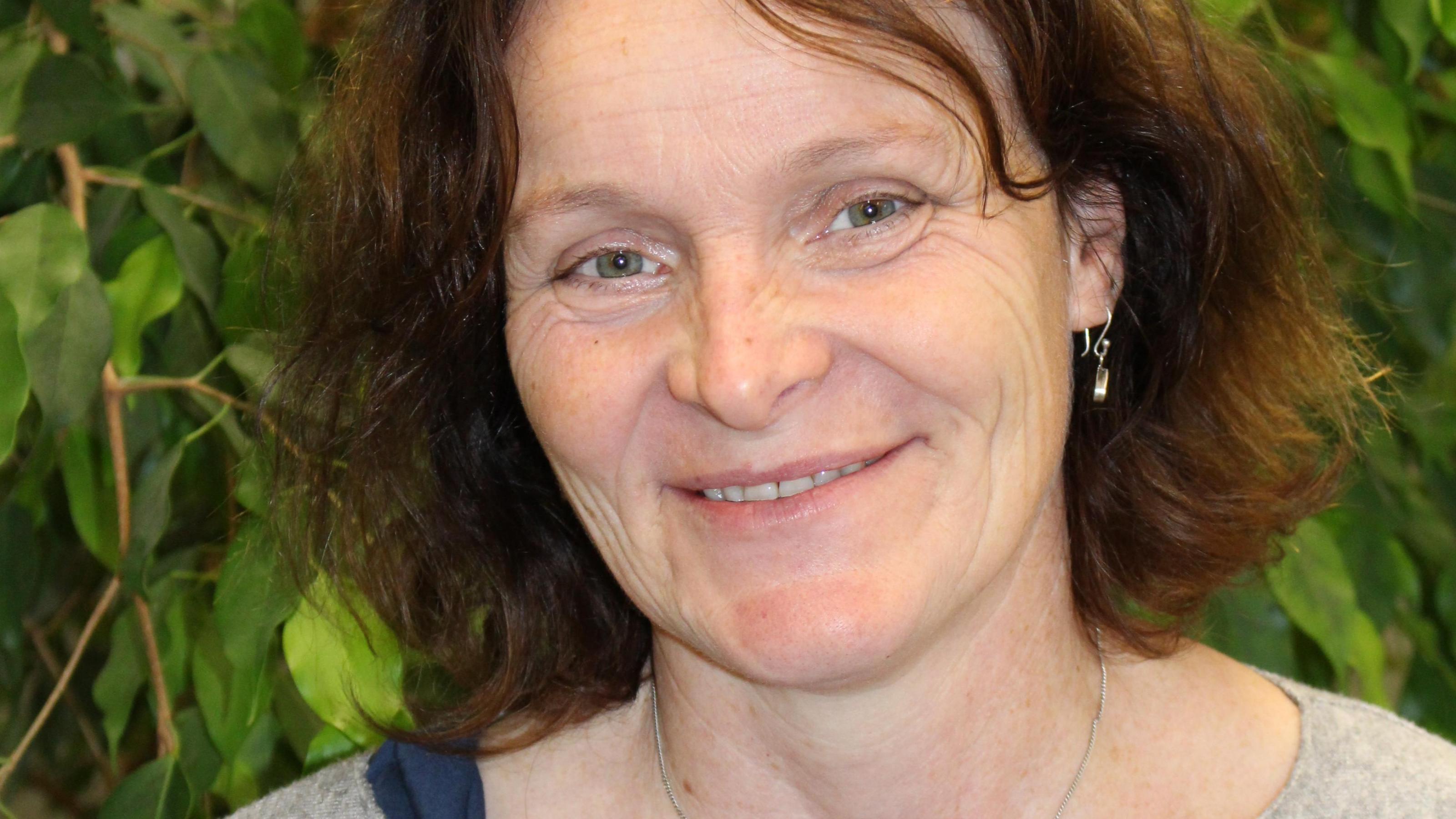 Portraitaufnahme Claudia Gester, grüne Blätter im Hintergrund.